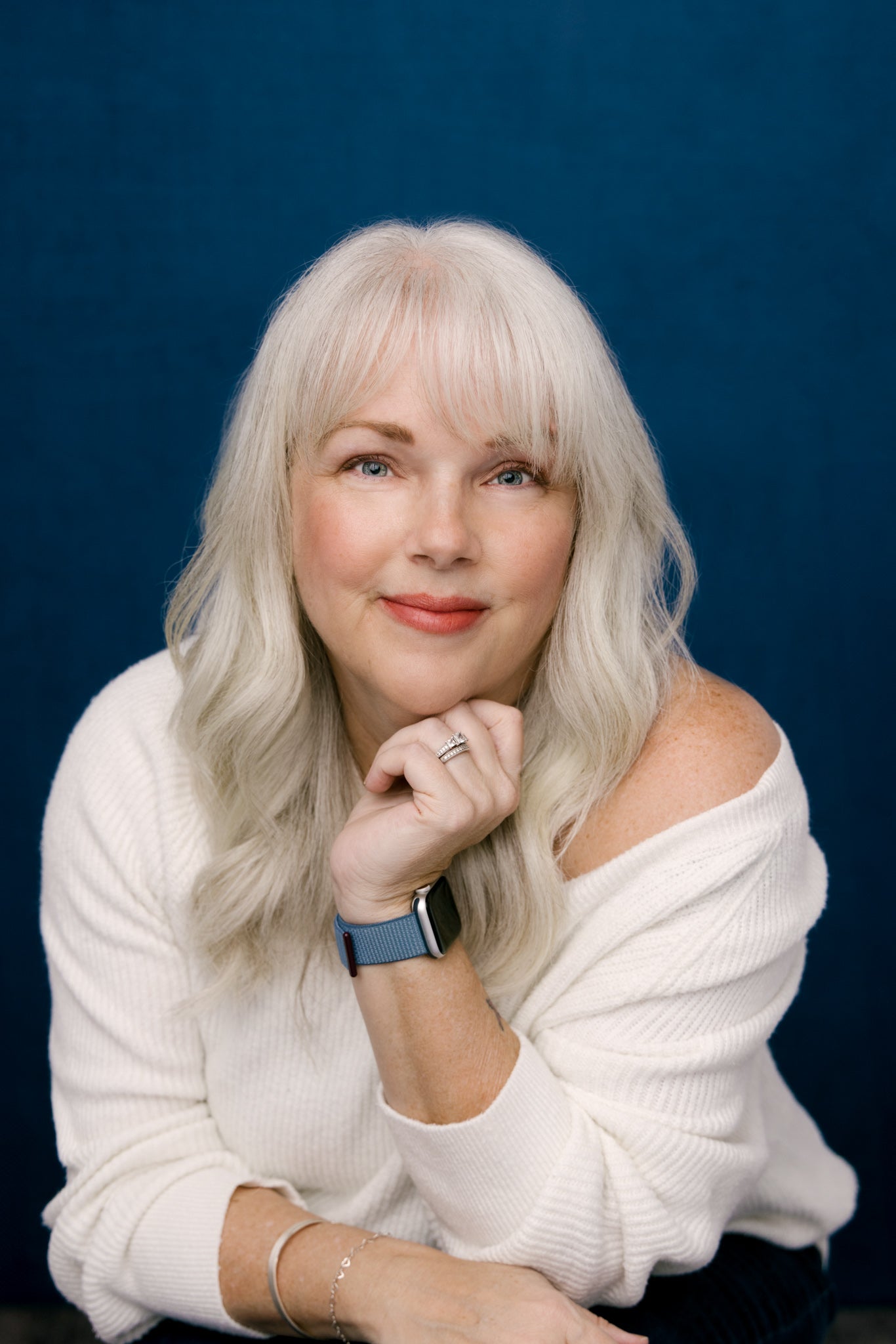 Woman with white hair wearing a white sweater against a blue background