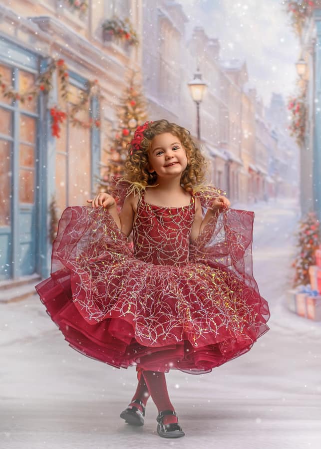 A young girl in a burgundy flower girl dress with a petticoat, standing in a room with a Christmas-themed backdrop.