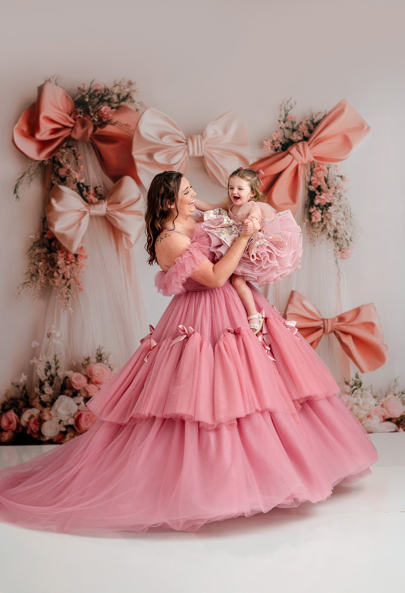 Elegant floor-length gown featuring a fitted bodice with intricate bow details and a flowing skirt. The gown is designed for adults sizes 6-12, made from high-quality satin and tulle, perfect for formal occasions, pageants, or photoshoots.