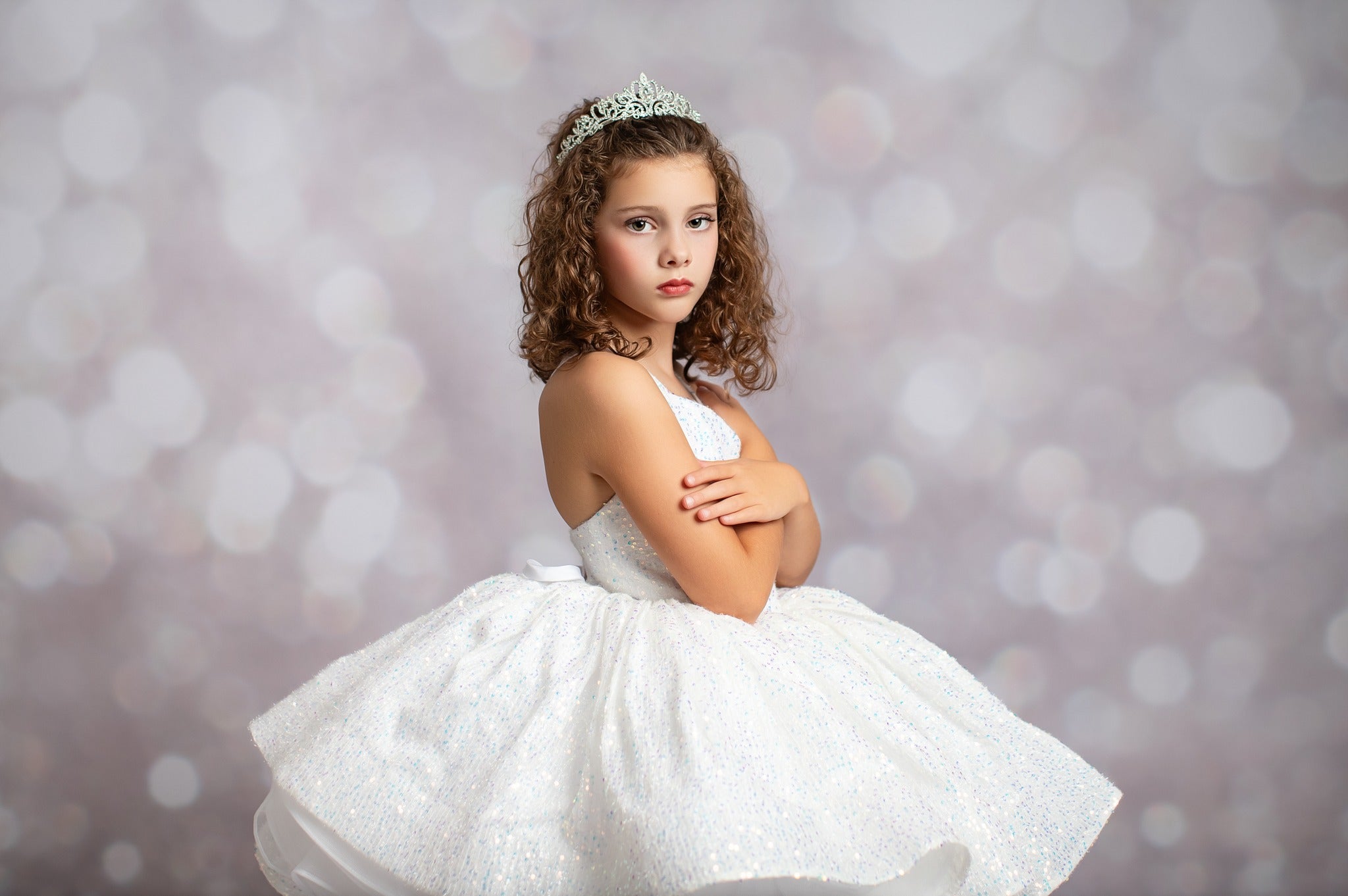 Young girl in a white dress with a tiara against a blurred light background