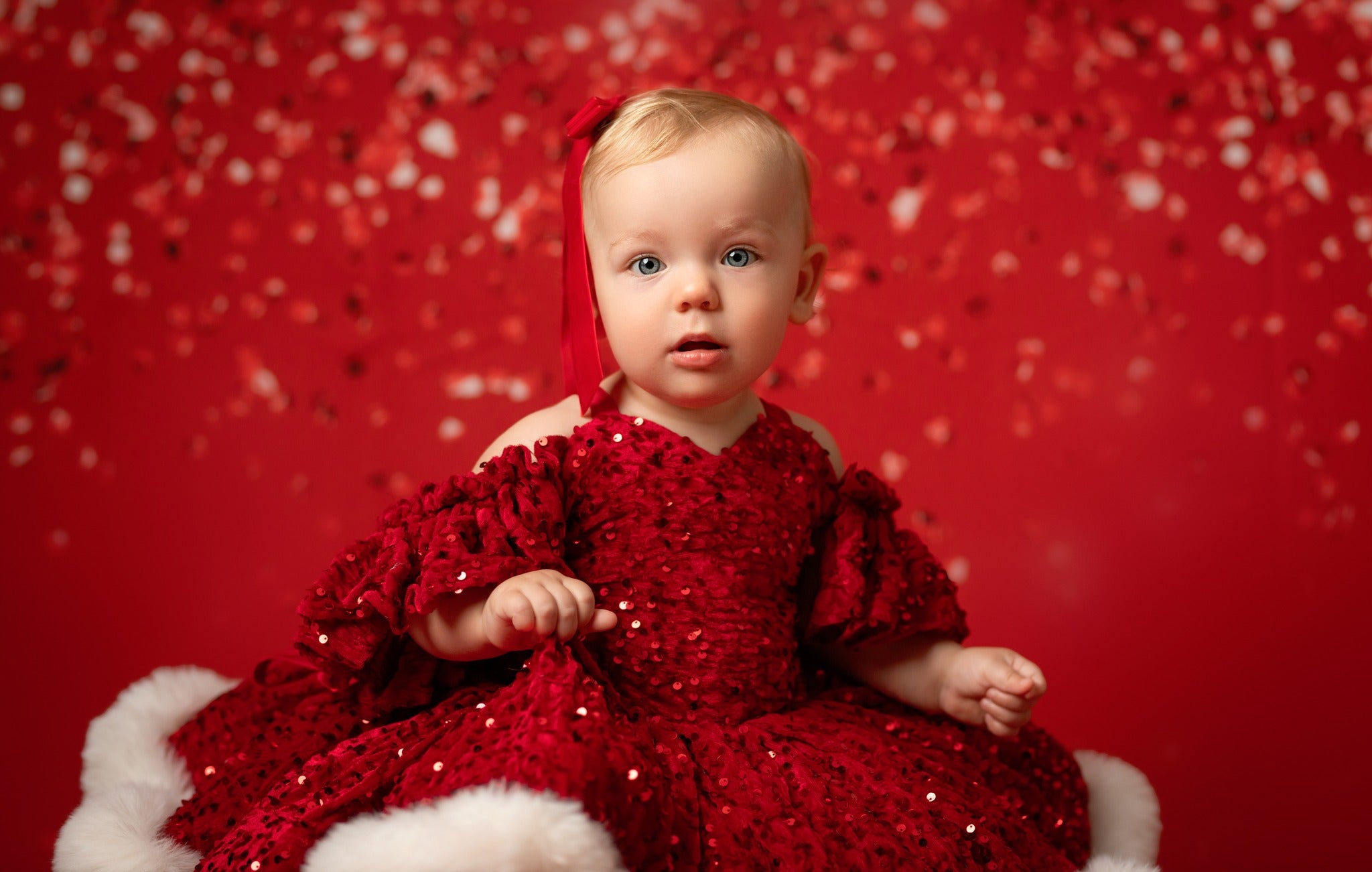 Baby in a red sequin dress sitting on a red background with snowflake patterns