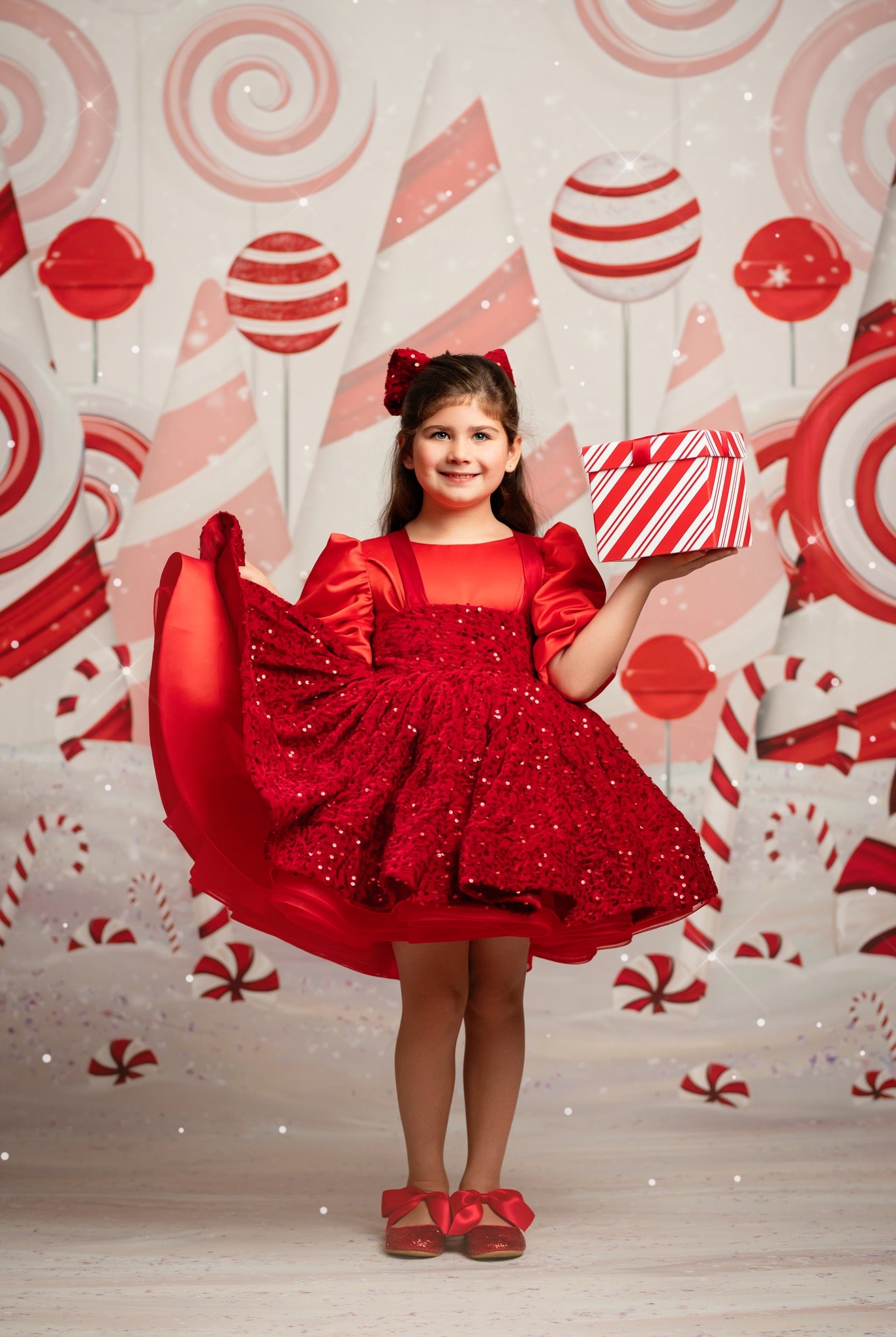 Young girl in a red dress holding a gift box against a candy-themed backdrop