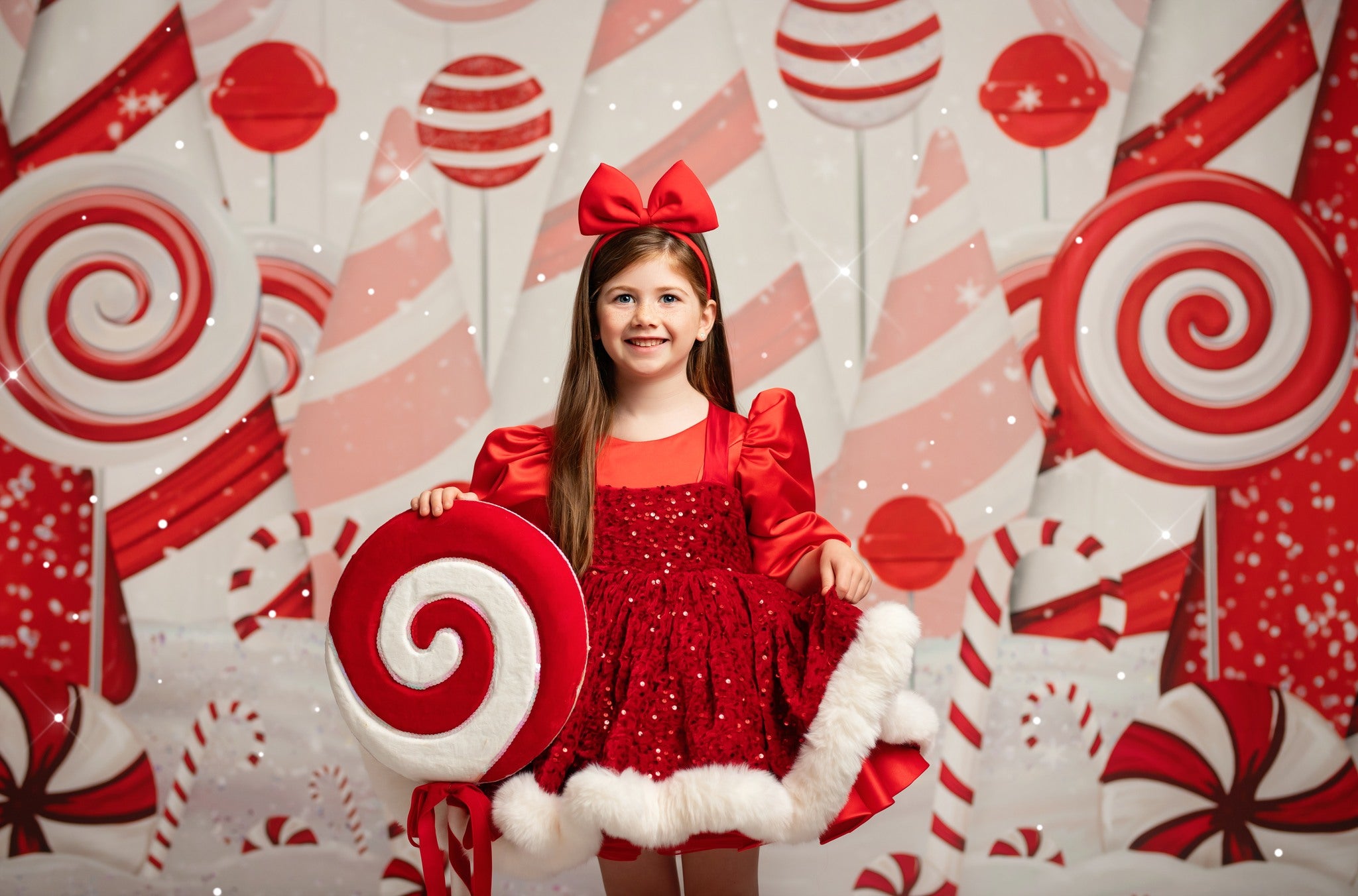 Young girl in a red dress with a large bow posing in front of a candy-themed background