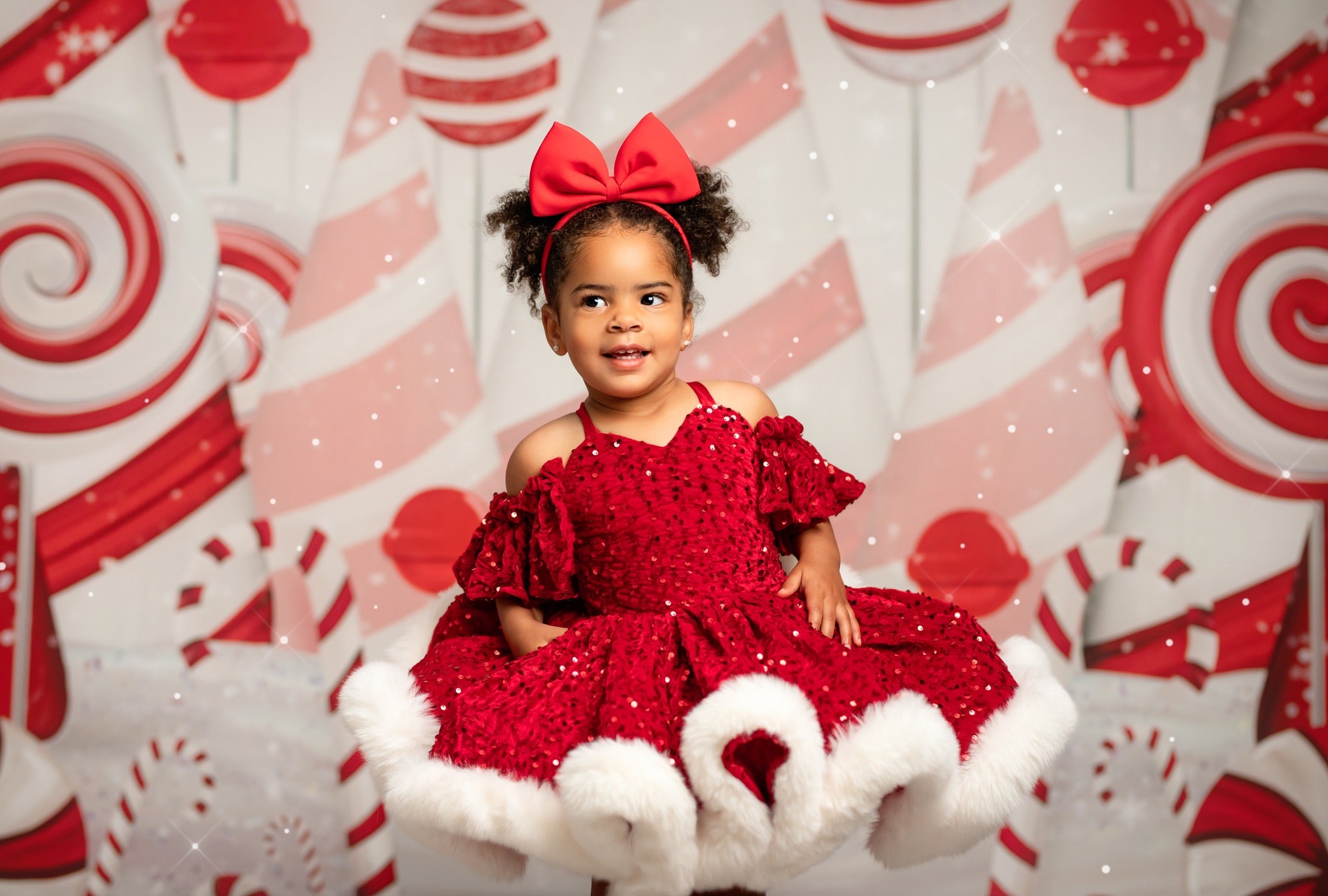 Child in a red dress with a large bow sitting in front of a candy-themed background