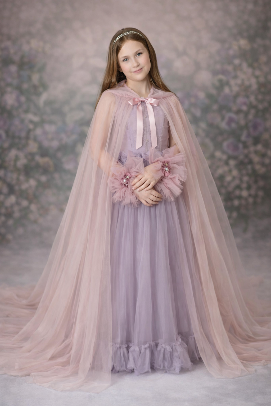 Young girl in a lavender dress with a pink cape and floral accessories against a floral backdrop