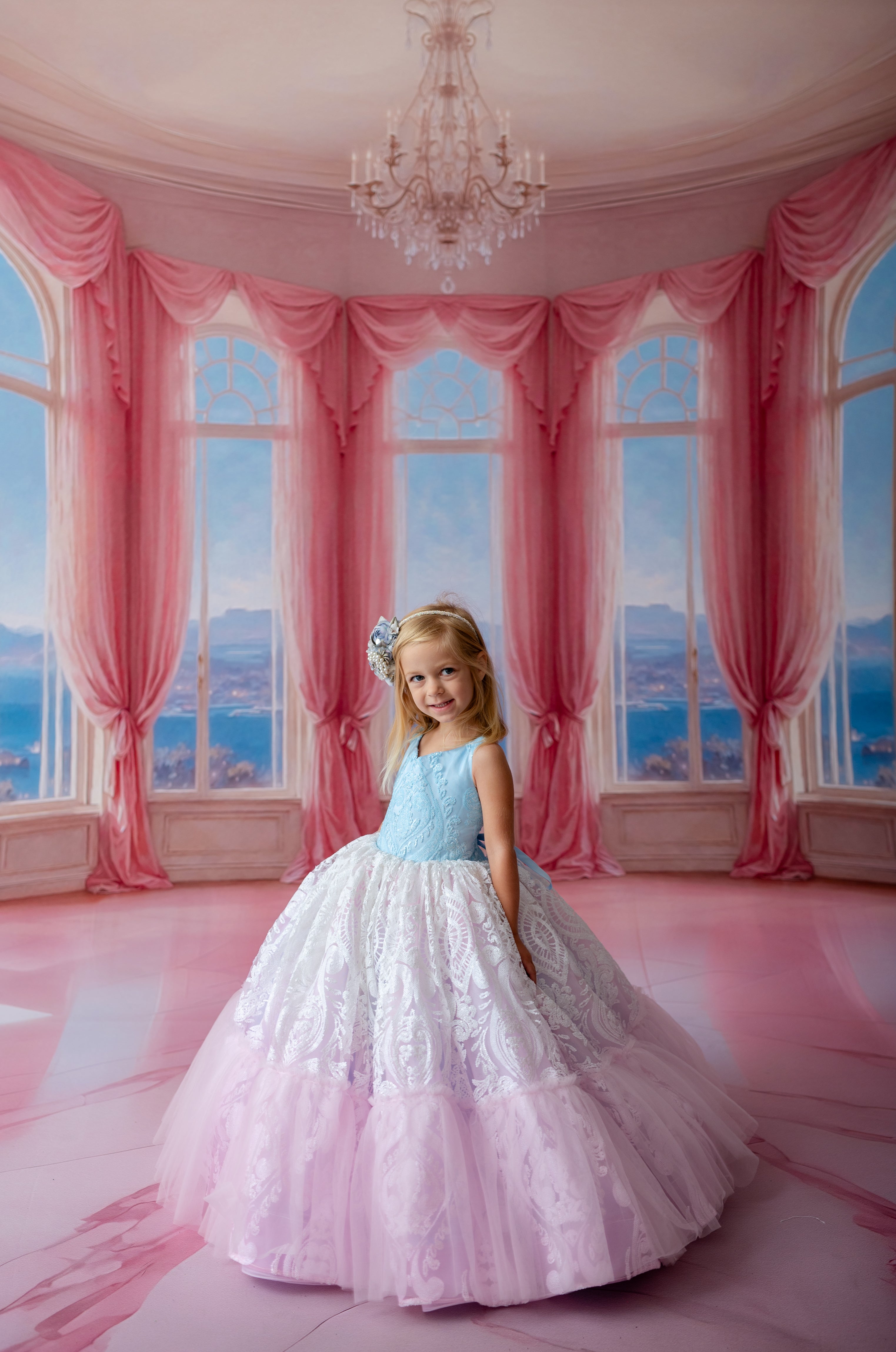 Young girl in a pink and white dress standing in a room with pink curtains and a chandelier.