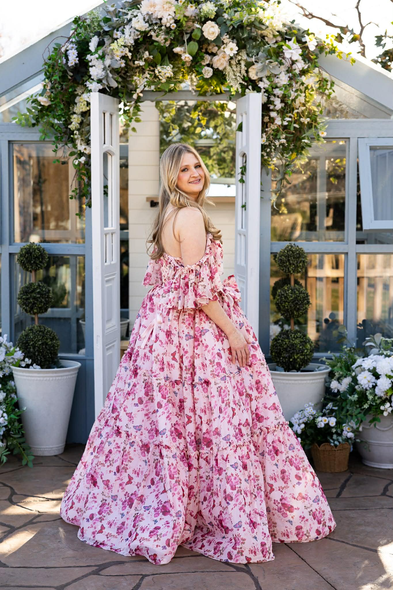 Woman in a floral dress standing in front of a decorated archway with flowers.