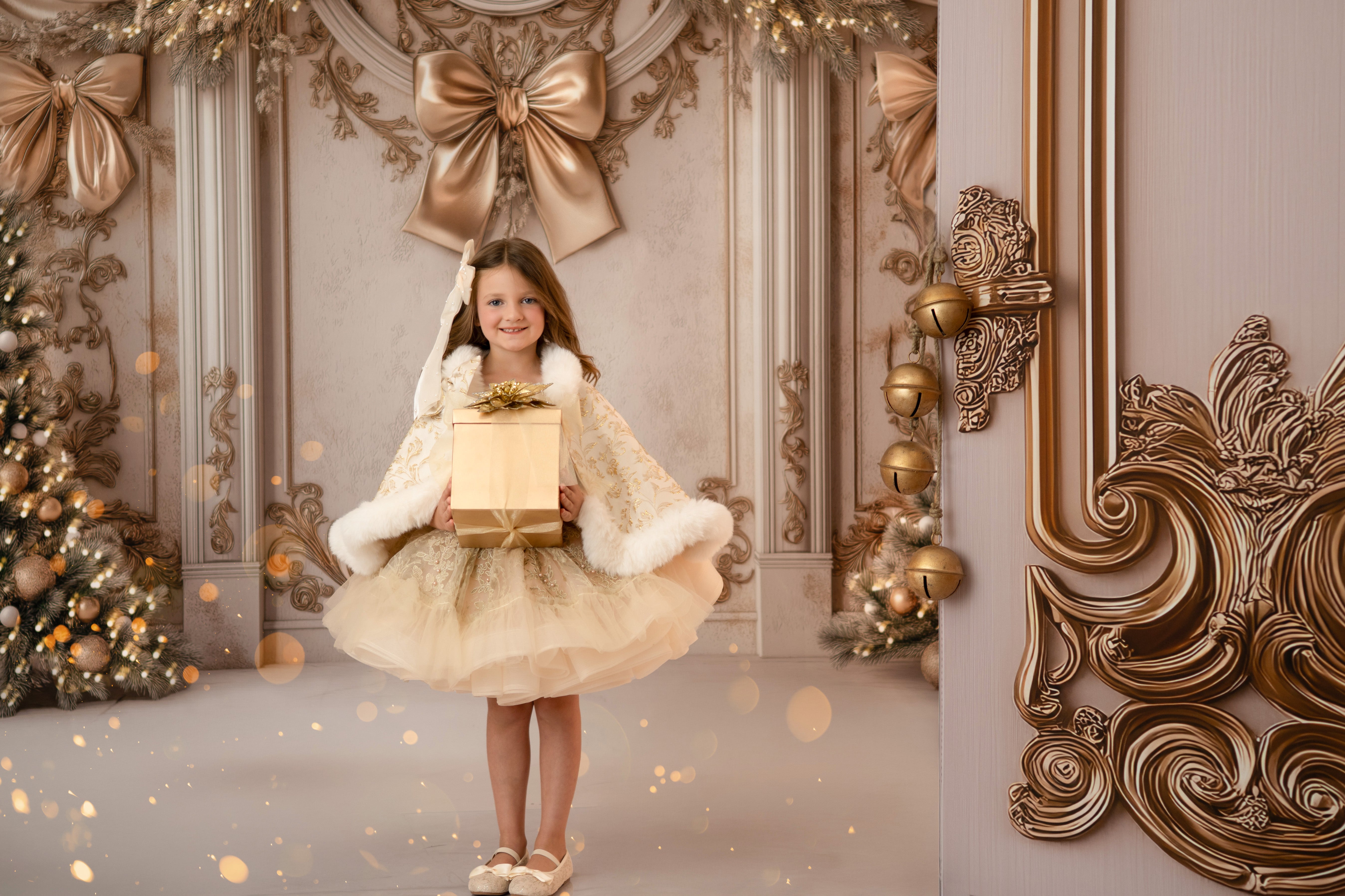Young girl in a gold dress holding a gift in a decorated room with ornate wall designs and Christmas trees.