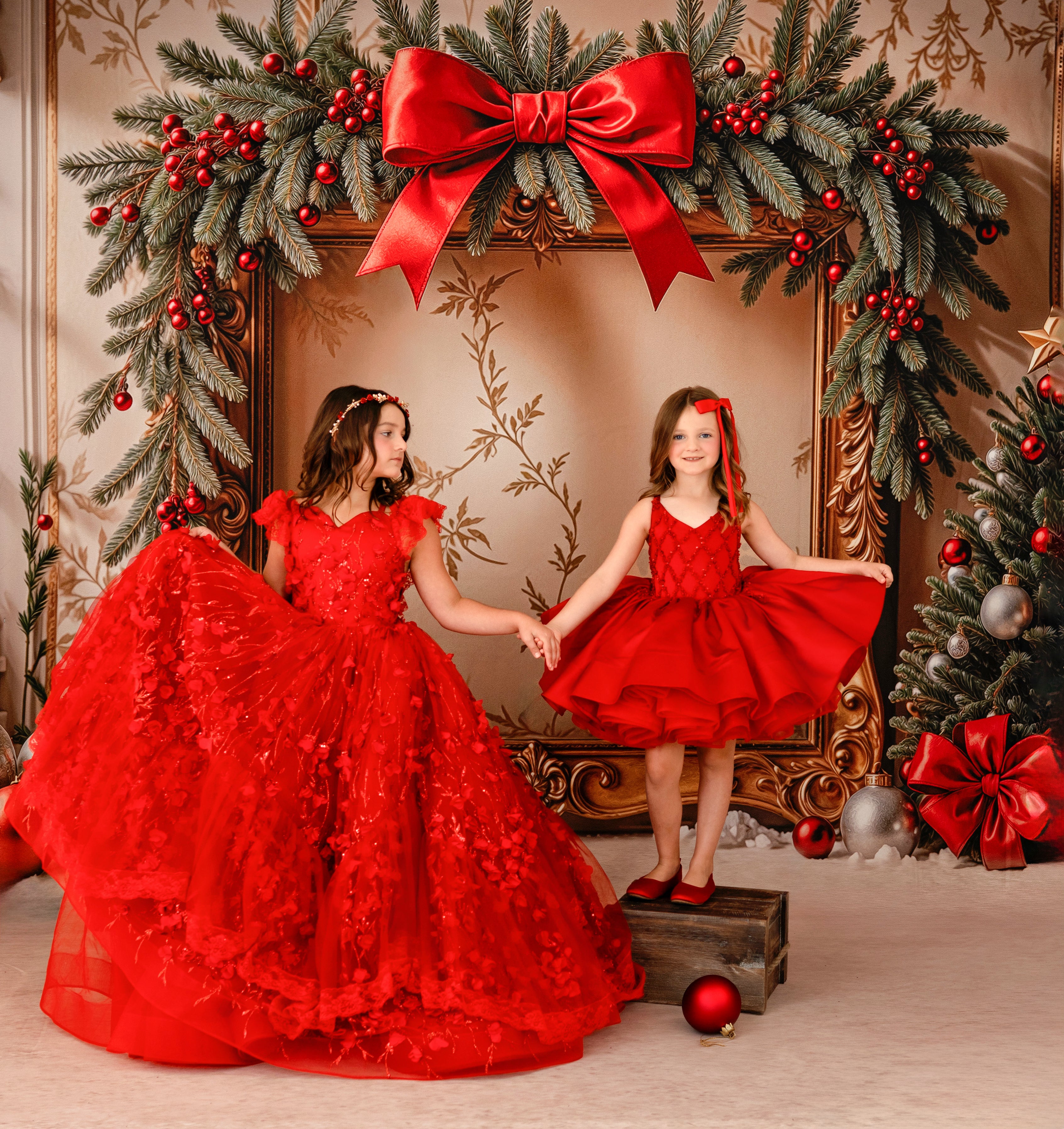 Two girls in red dresses standing in front of a decorated Christmas fireplace.