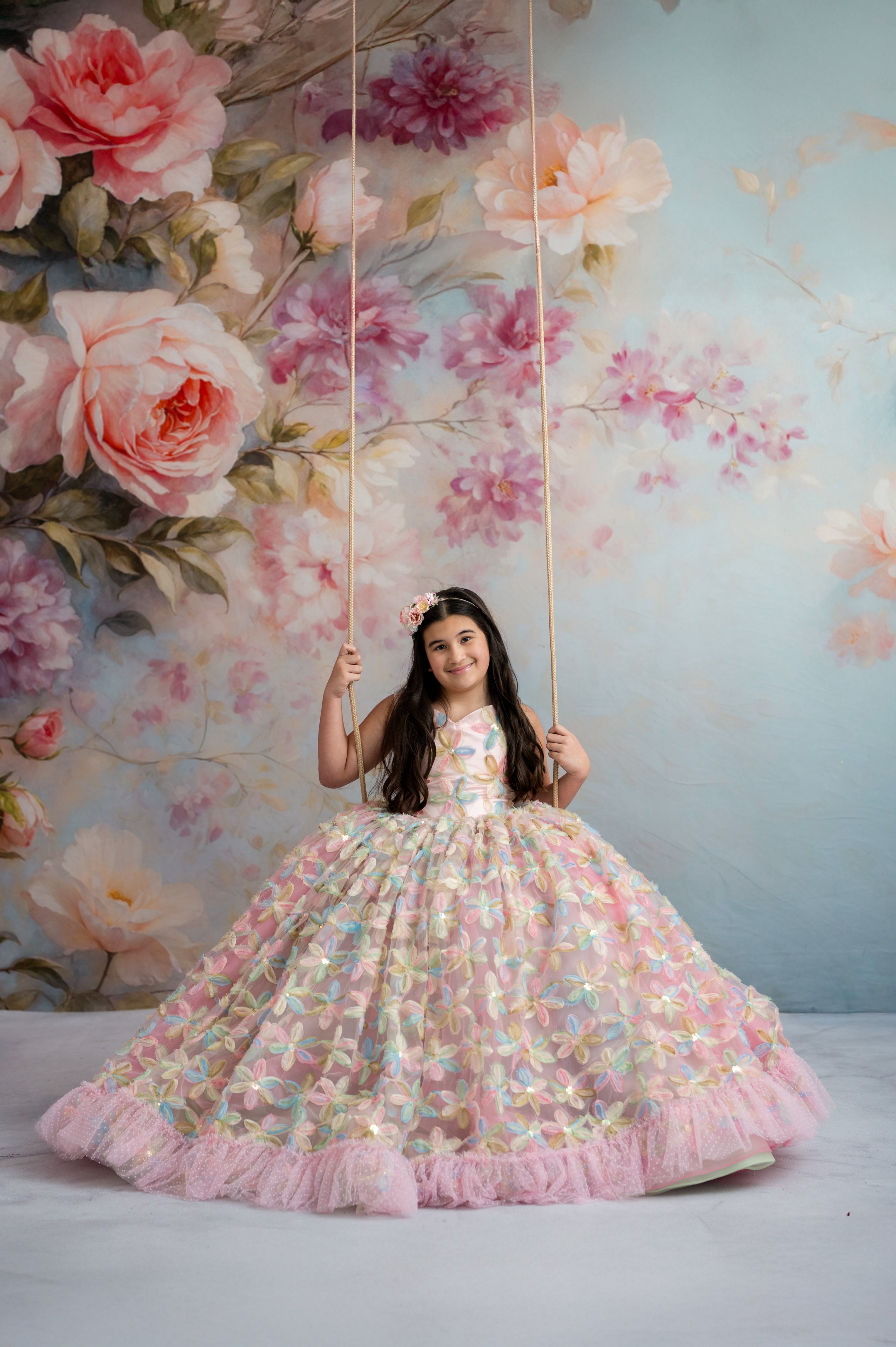 Young girl in a floral dress on a swing against a floral wall backdrop