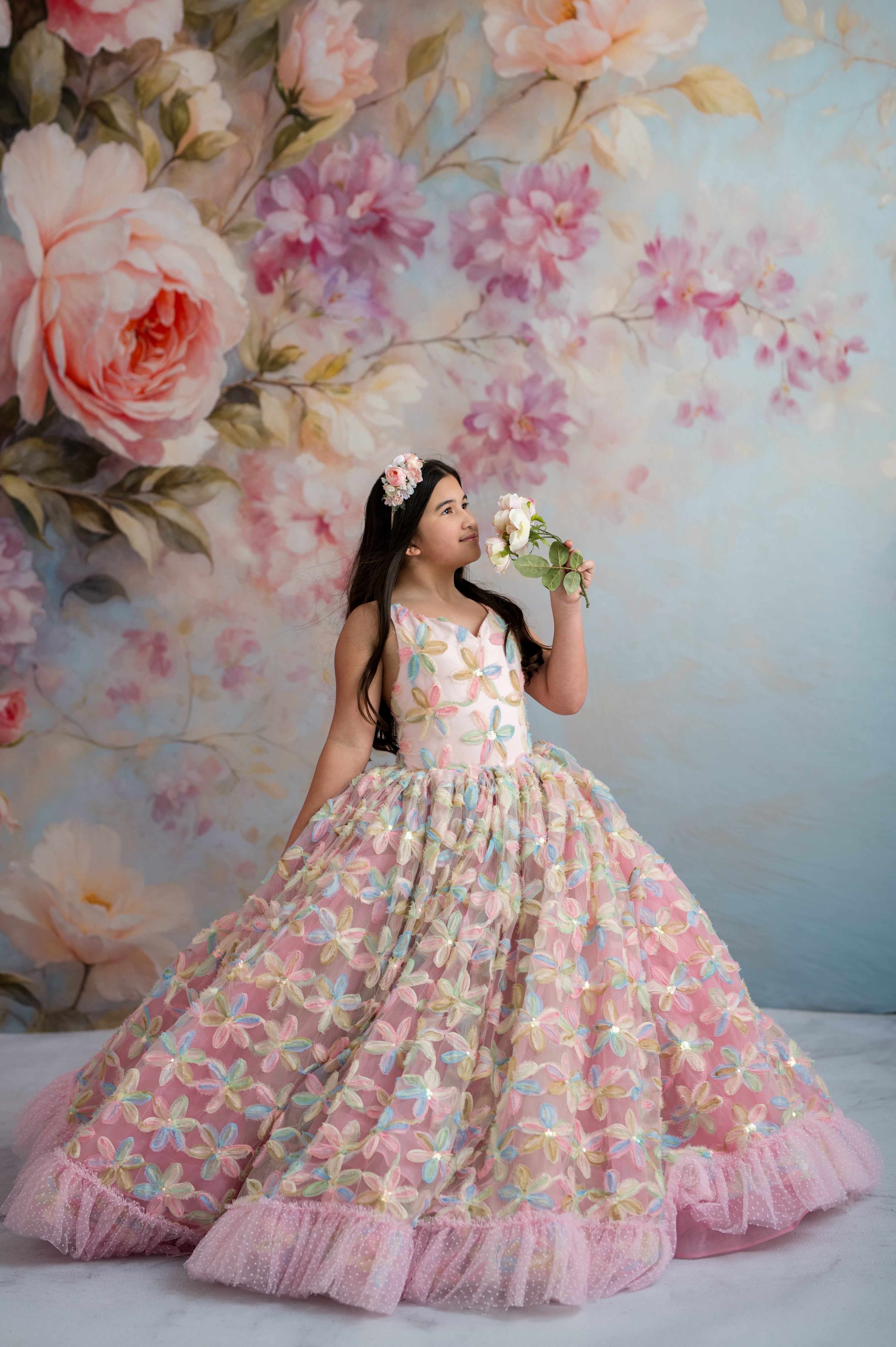 Young girl in a floral dress standing against a floral backdrop