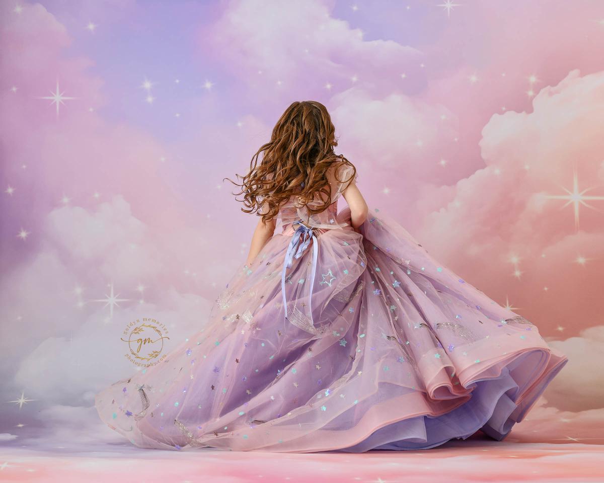 "A charming young girl wearing a celestial-themed gown with layered tulle, standing in front of a pastel starry backdrop."