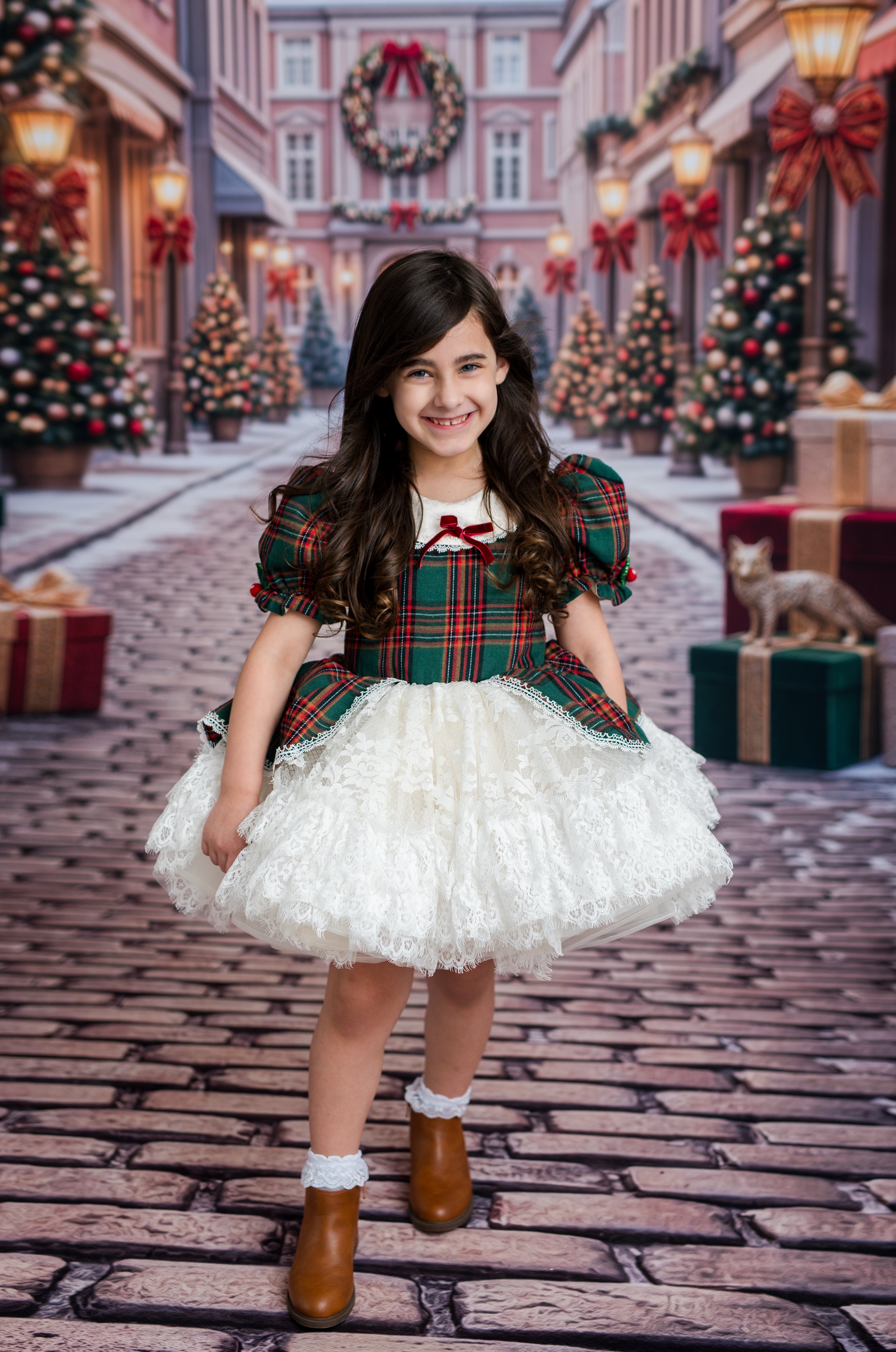 A young girl stands in a festive Christmas town street wearing a holiday dress with a green and red plaid bodice, white ruffled skirt, brown boots, and white socks. The background shows decorated Christmas trees, wreaths, and gift boxes.