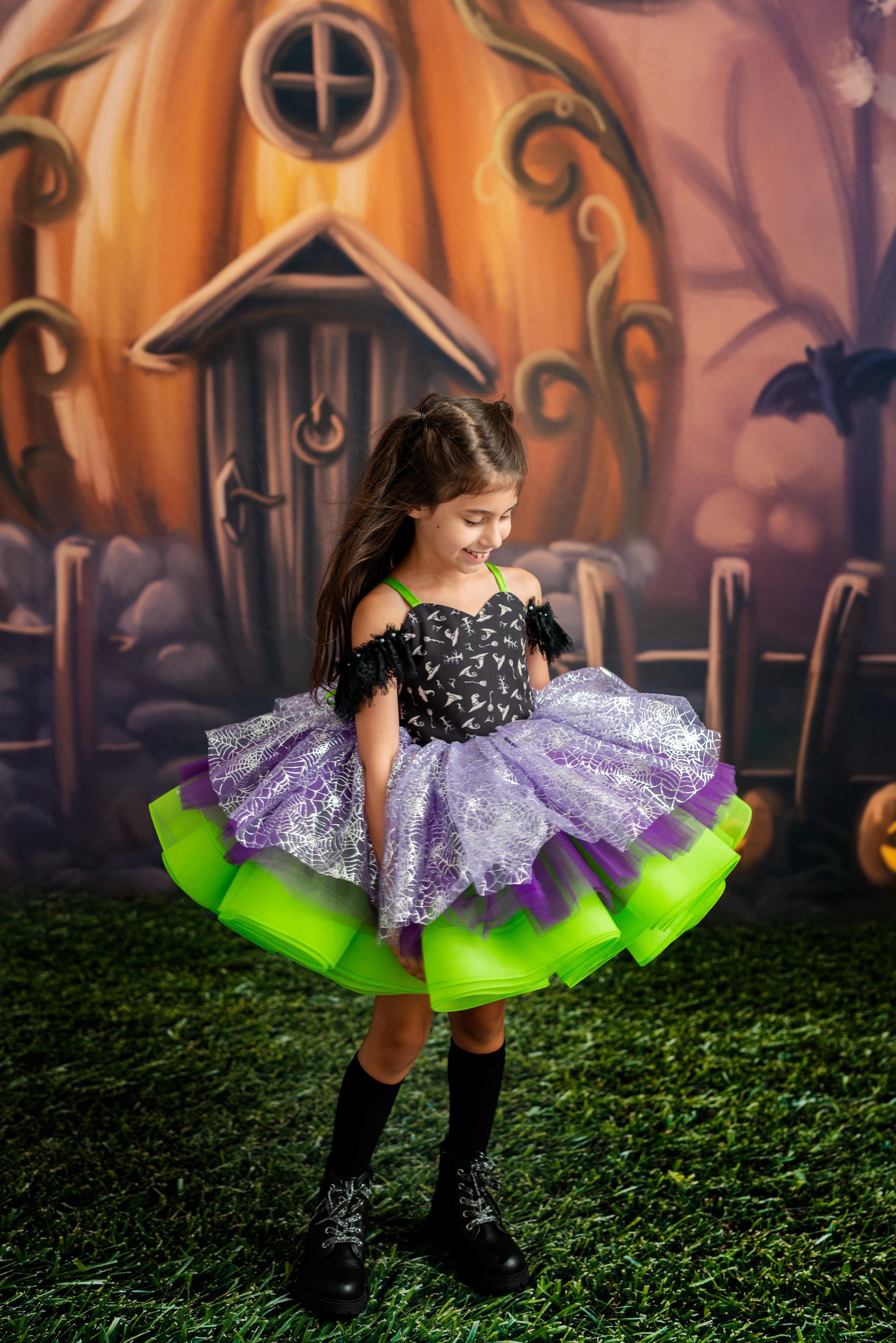 Child in a Halloween-themed costume standing in front of a pumpkin house backdrop