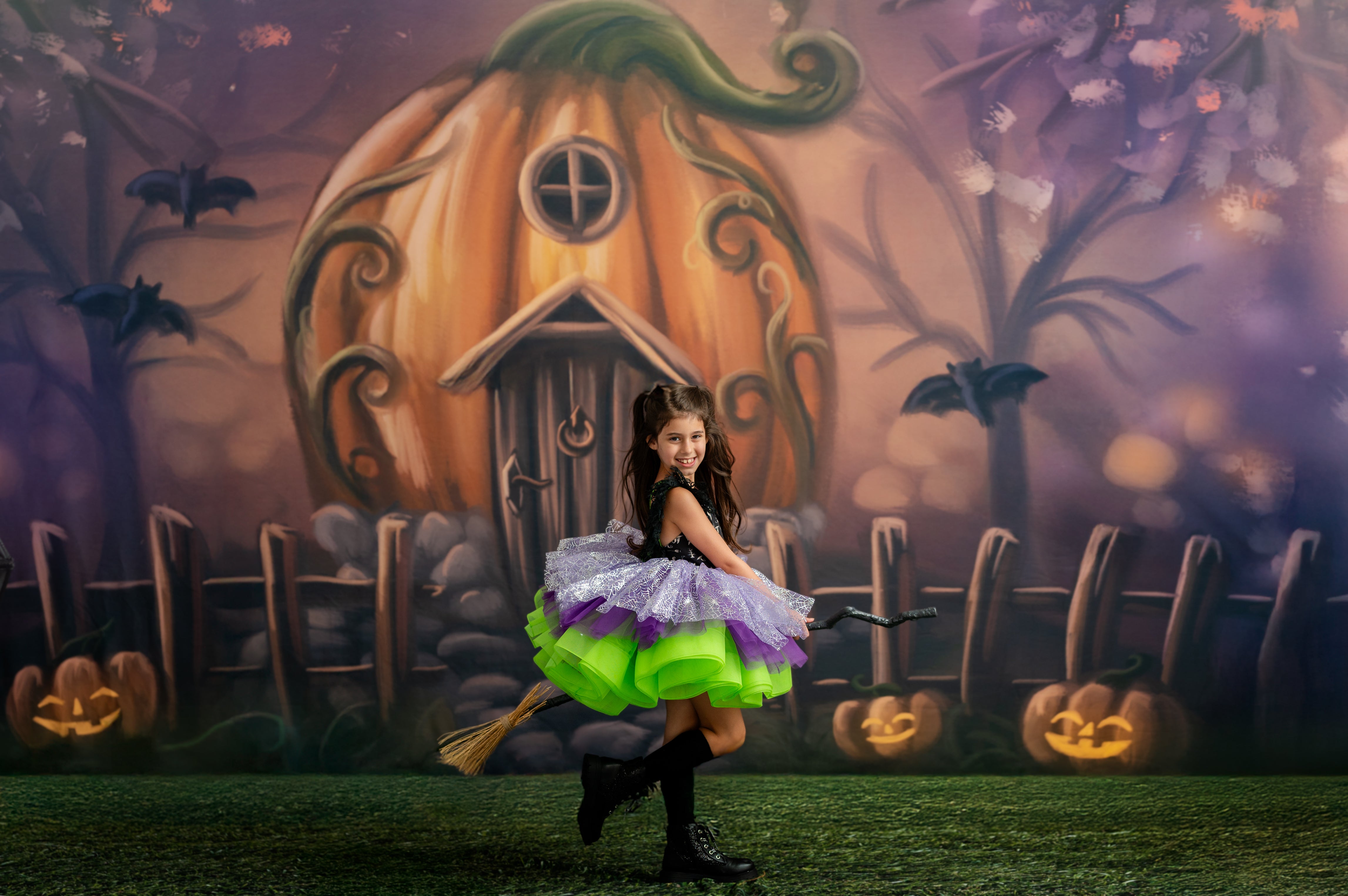 Woman in a colorful dress standing in front of a pumpkin house with Halloween-themed decorations.
