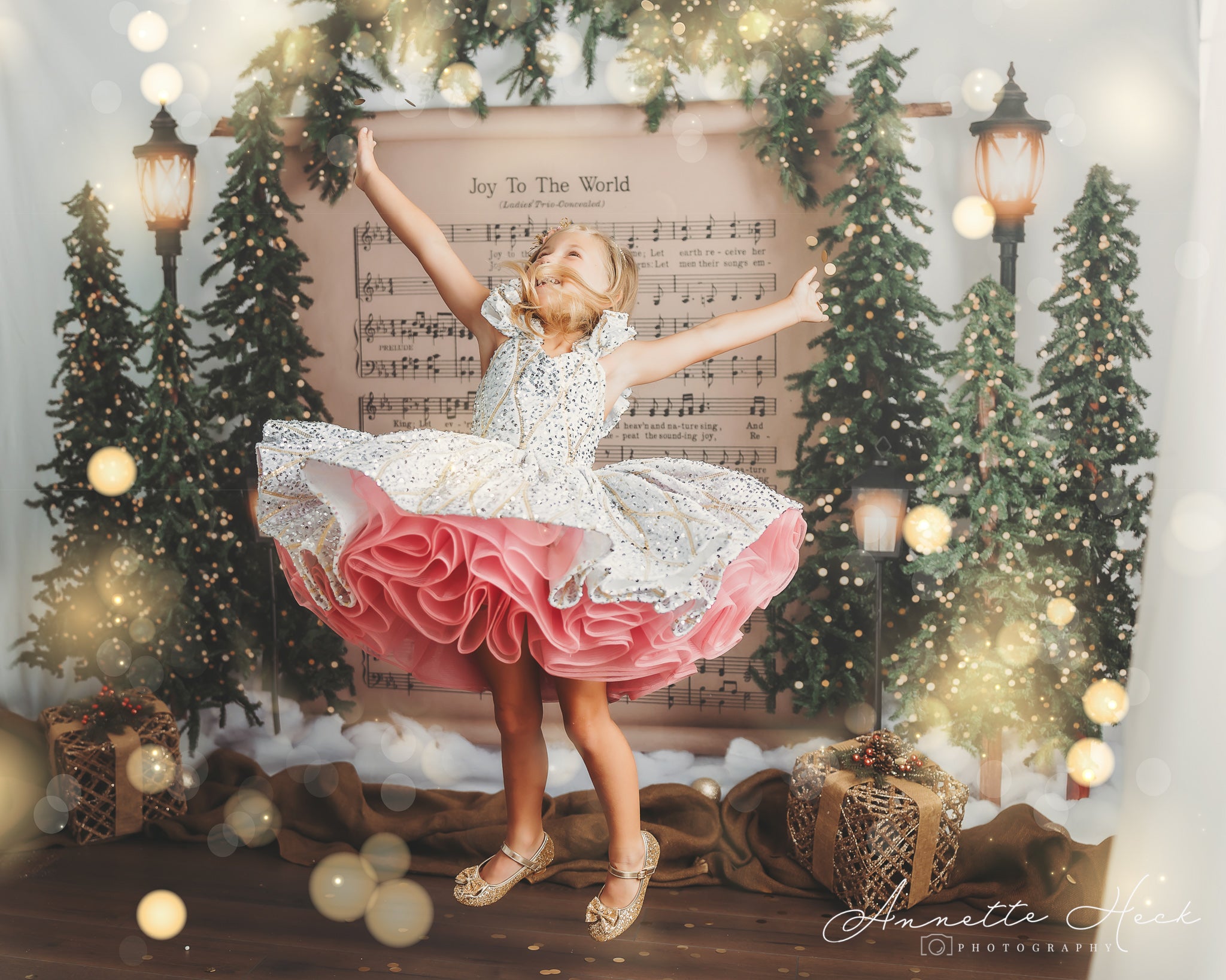 Child twirls in a sparkling gown with intricate details and a layered pink skirt, standing on a rustic wooden floor.