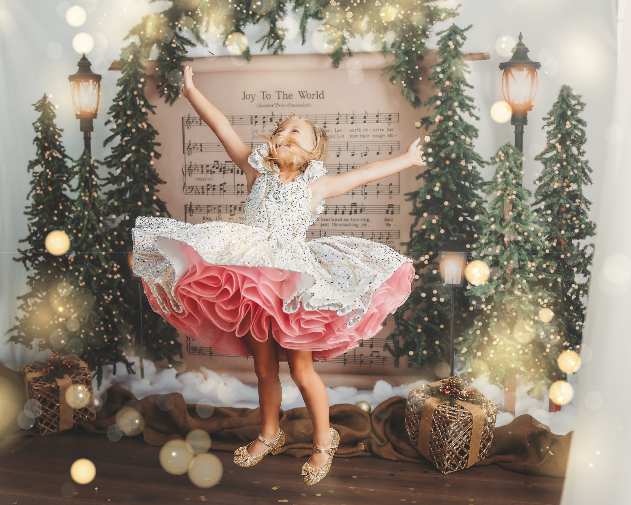 Young girl in a glittery dress with a pink ruffled petticoat, her arms extended as she gracefully spins in a soft-lit room.