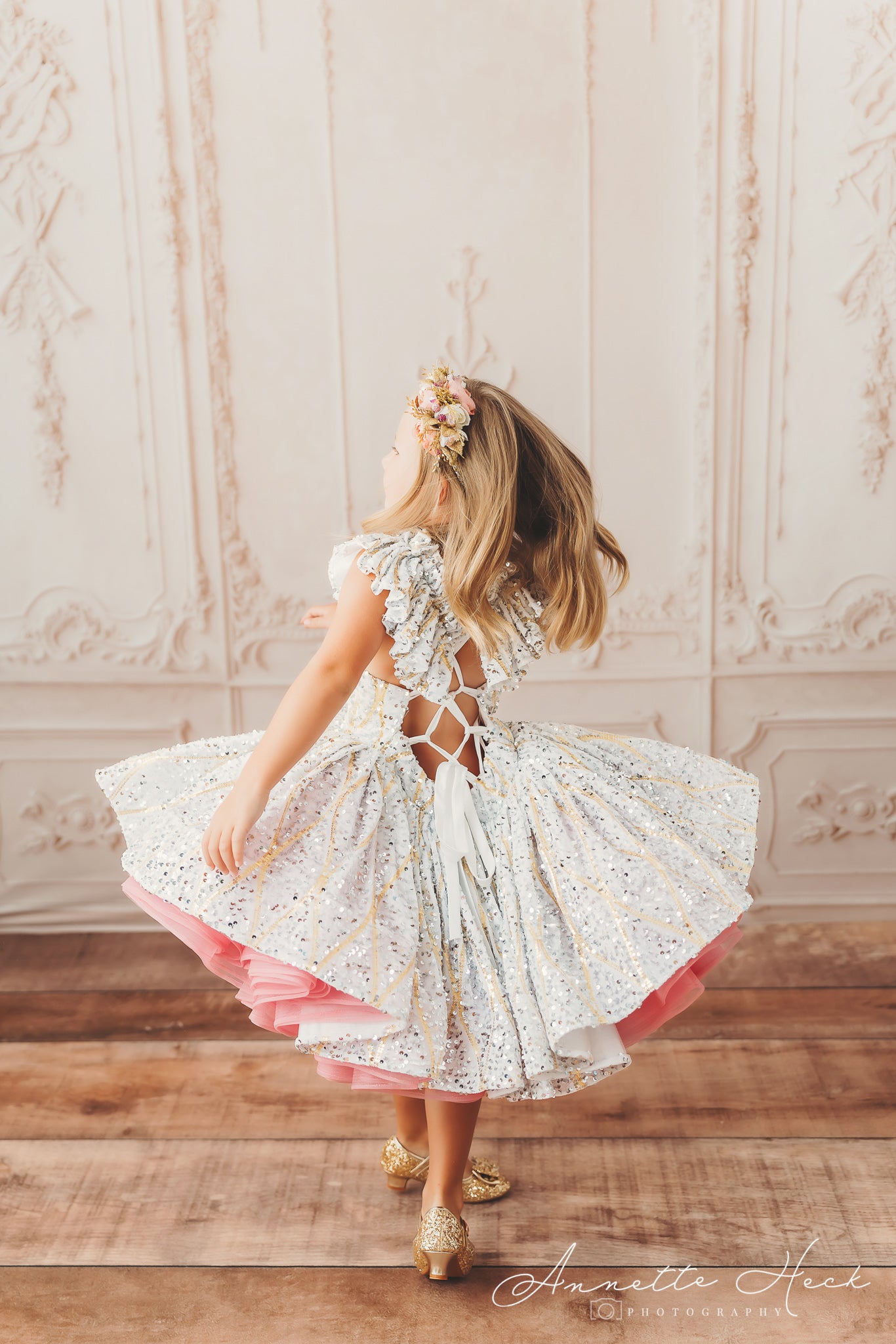 Girl dancing in a shimmering dress with gold details and pink ruffles peeking out from beneath the skirt.