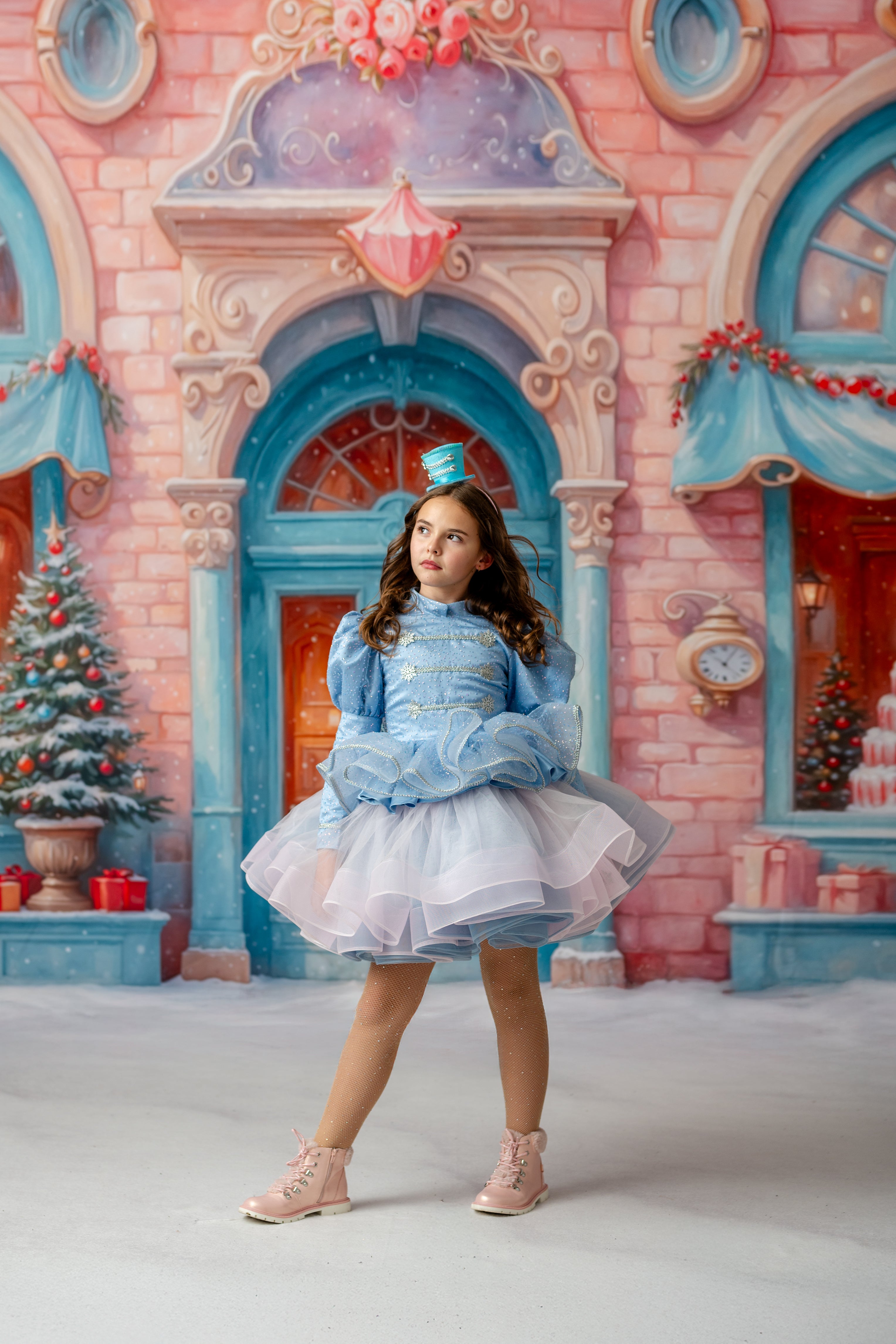Young girl in a blue dress standing in front of a festive castle backdrop.