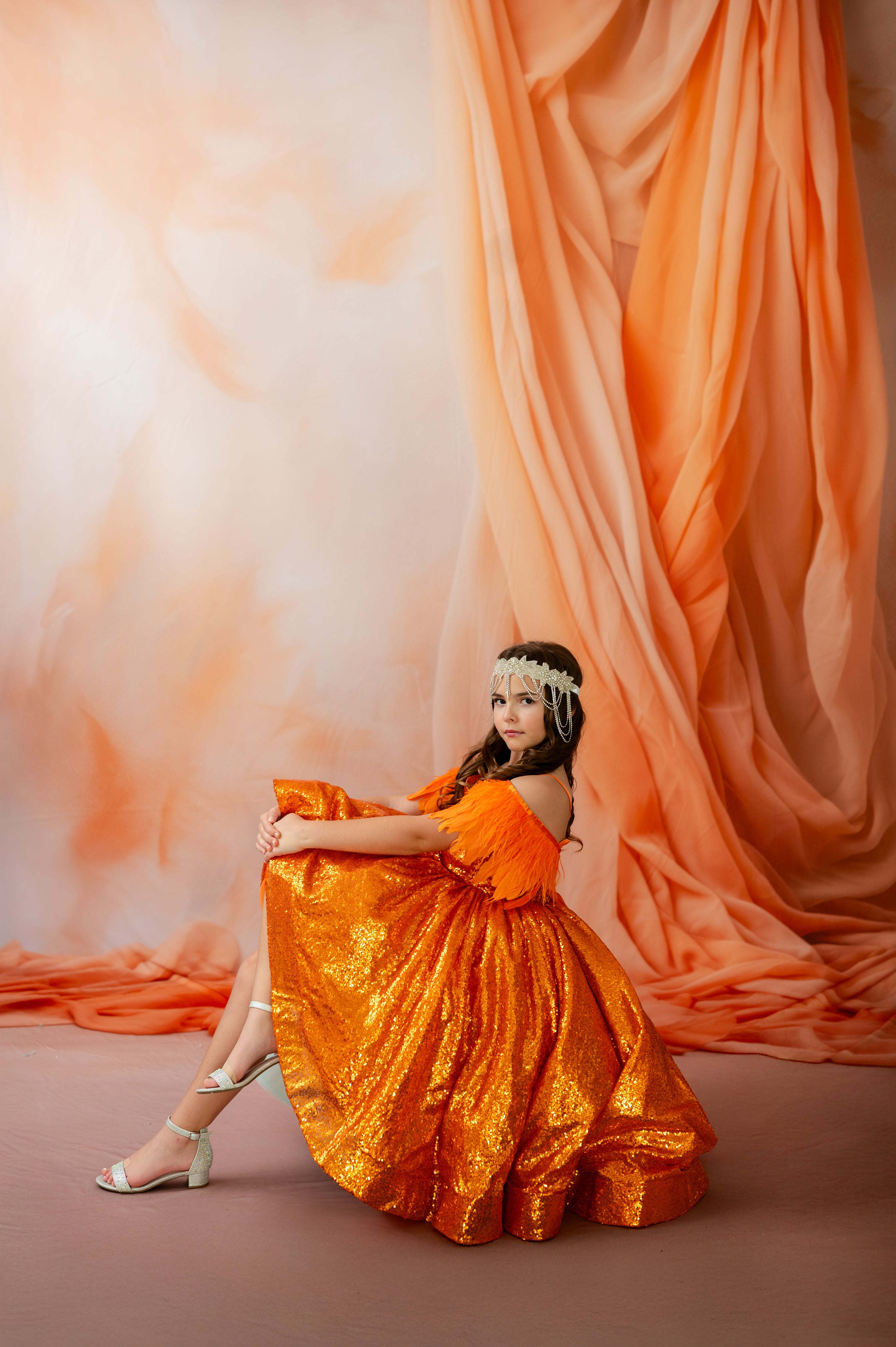 Woman in an orange dress sitting against a draped orange fabric backdrop