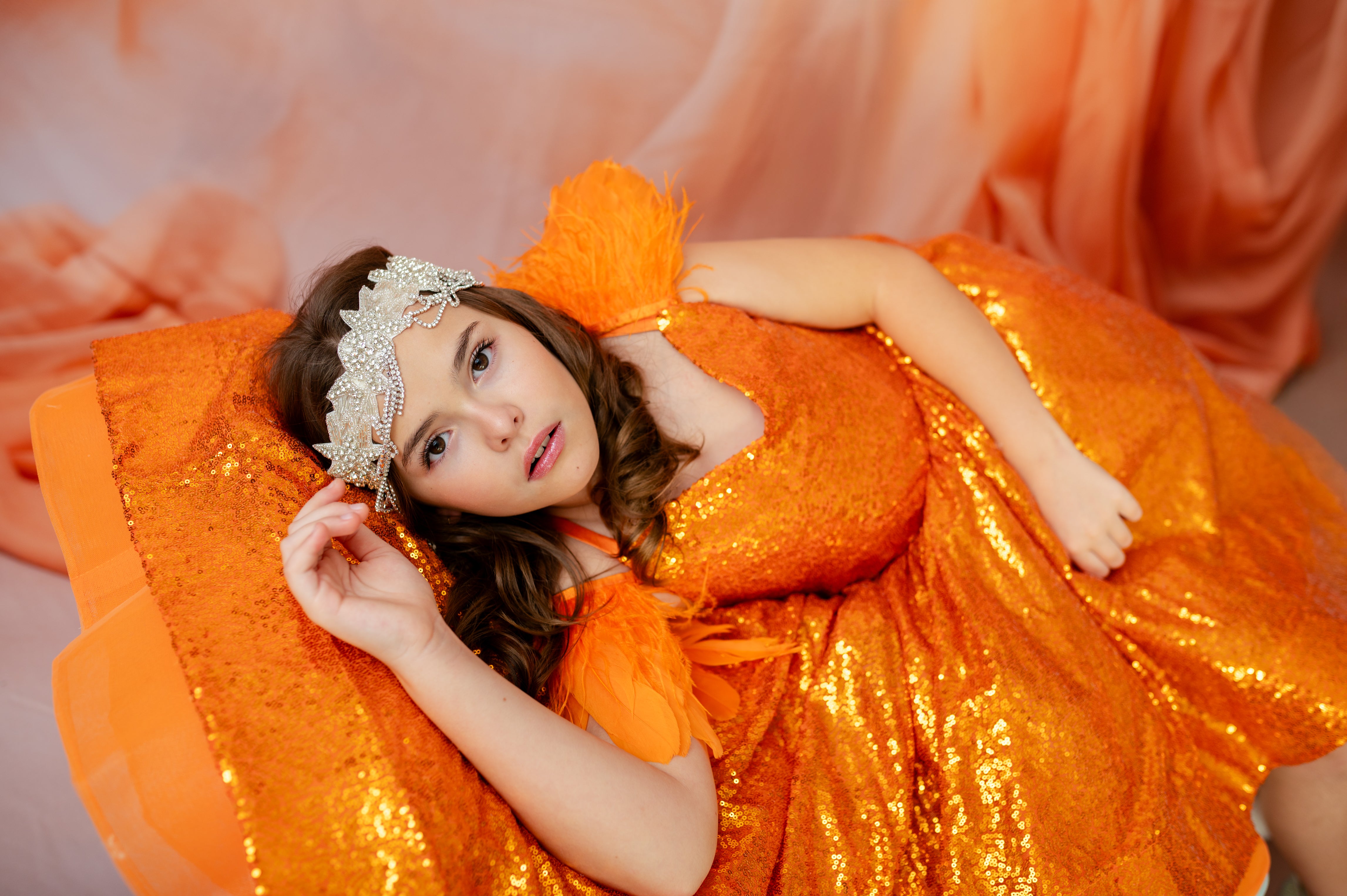 Woman in an orange sequin dress lying on a pink fabric background
