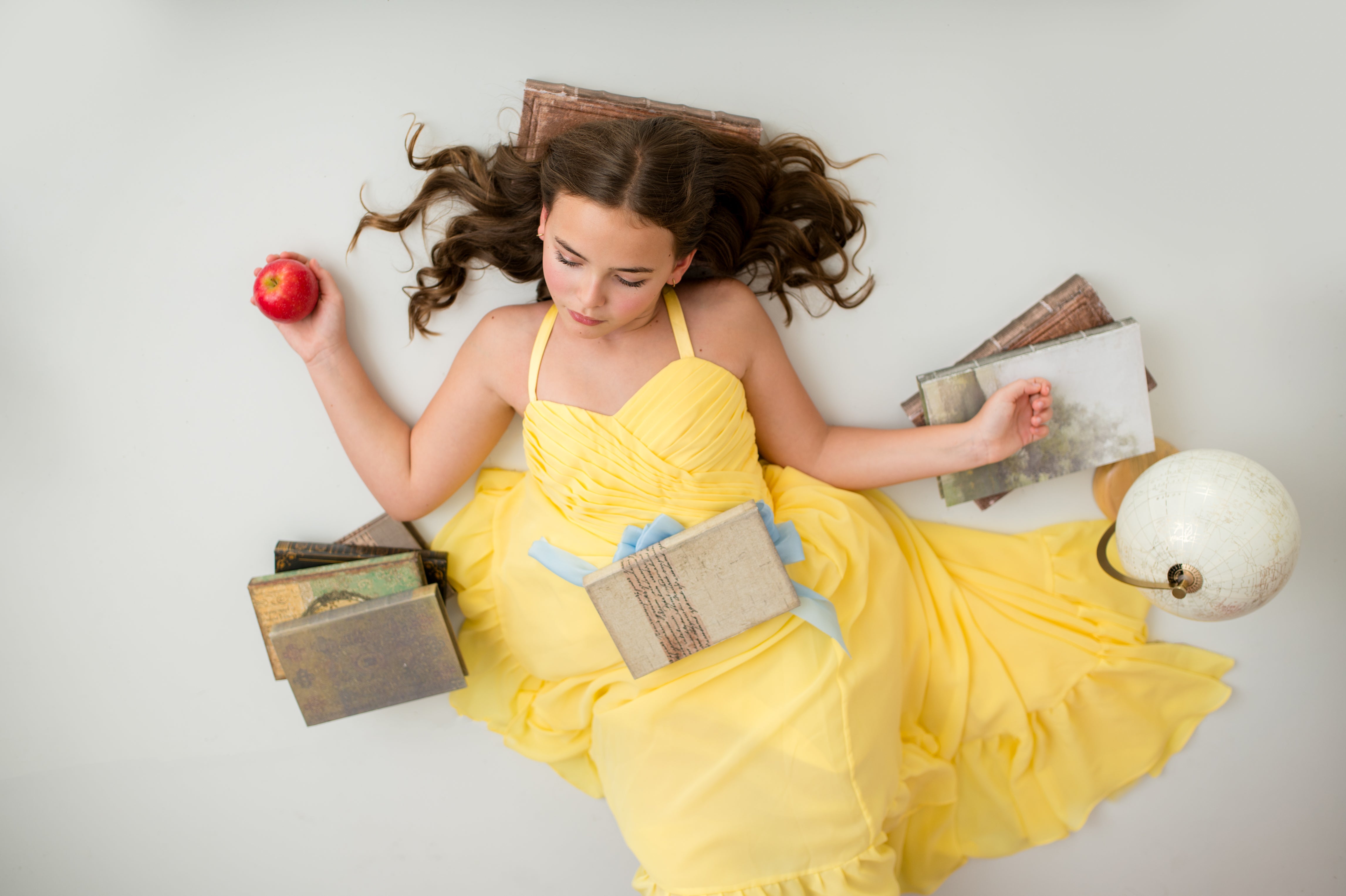 Woman in a yellow dress holding an apple and a book on a white background