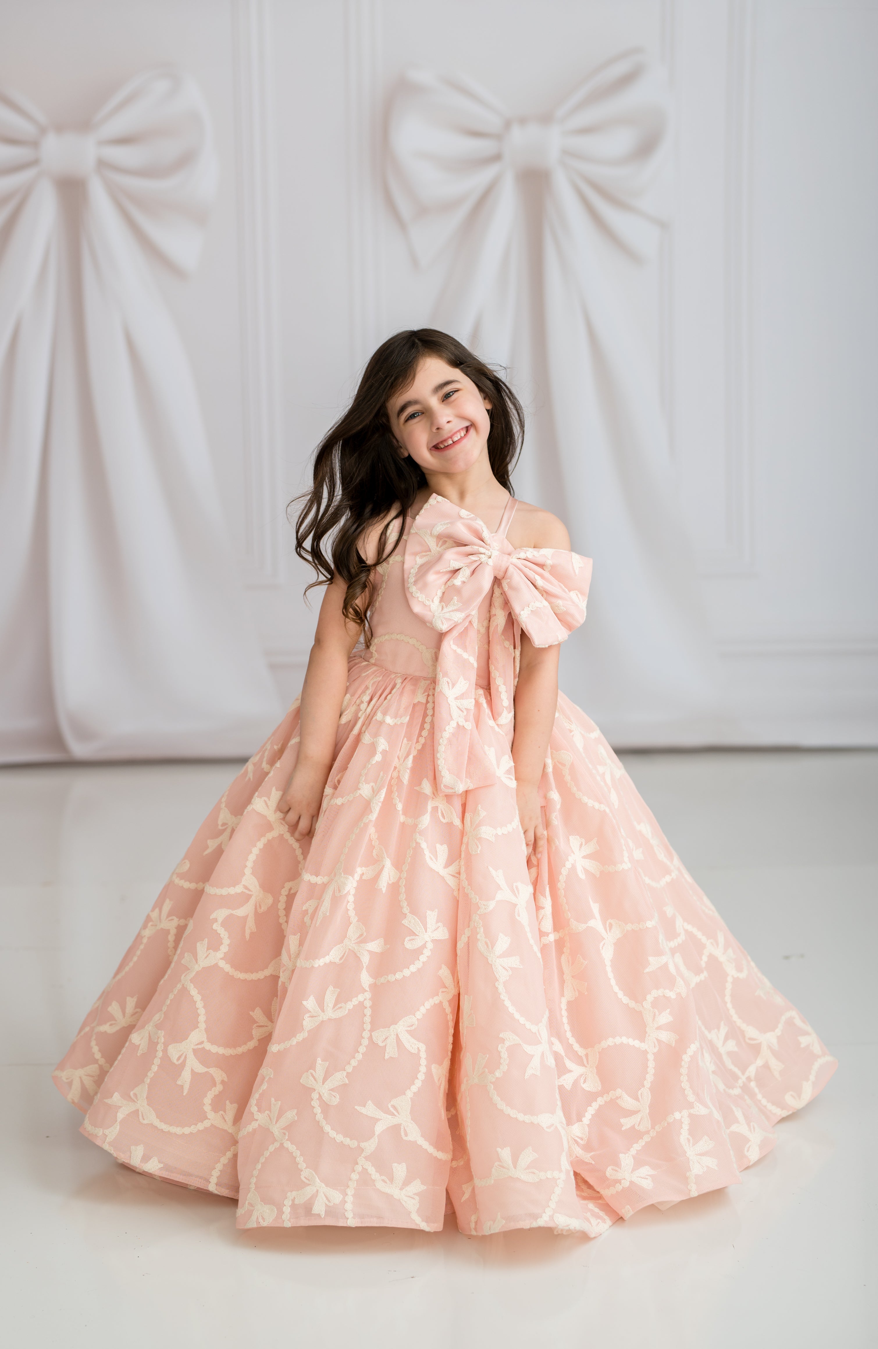 Young girl in a pink floral dress with a large bow standing against a white background