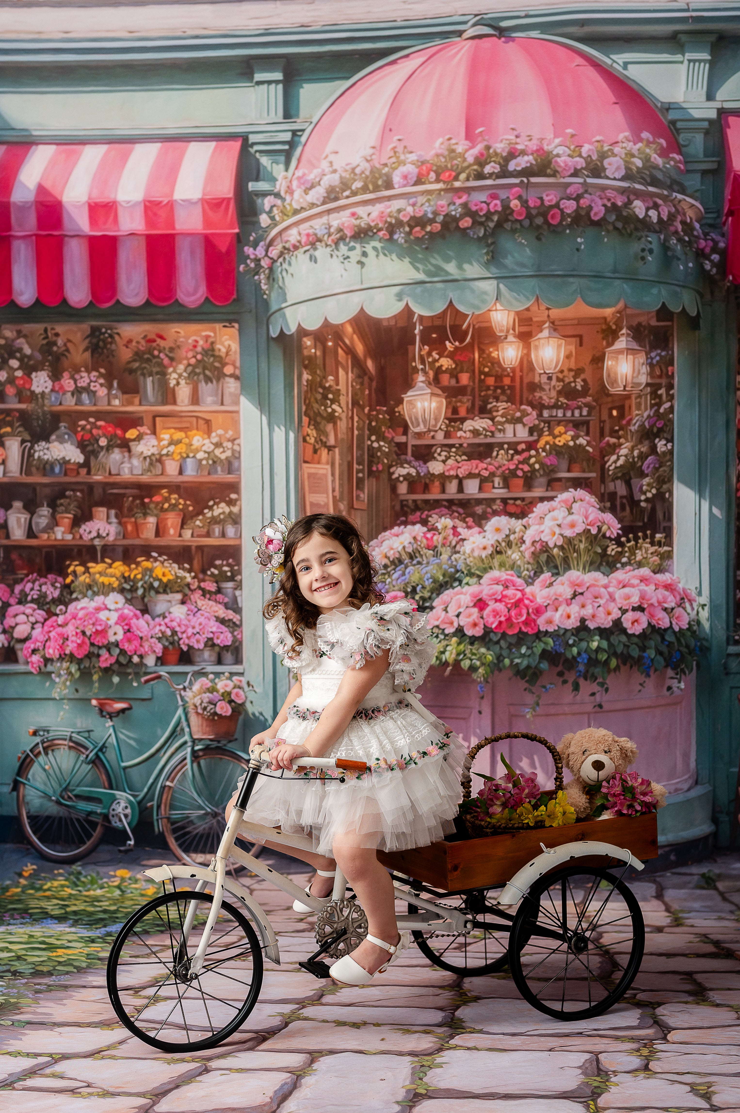 "A smiling young girl in a floral lace dress poses in front of a whimsical flower shop backdrop, surrounded by vibrant blossoms."