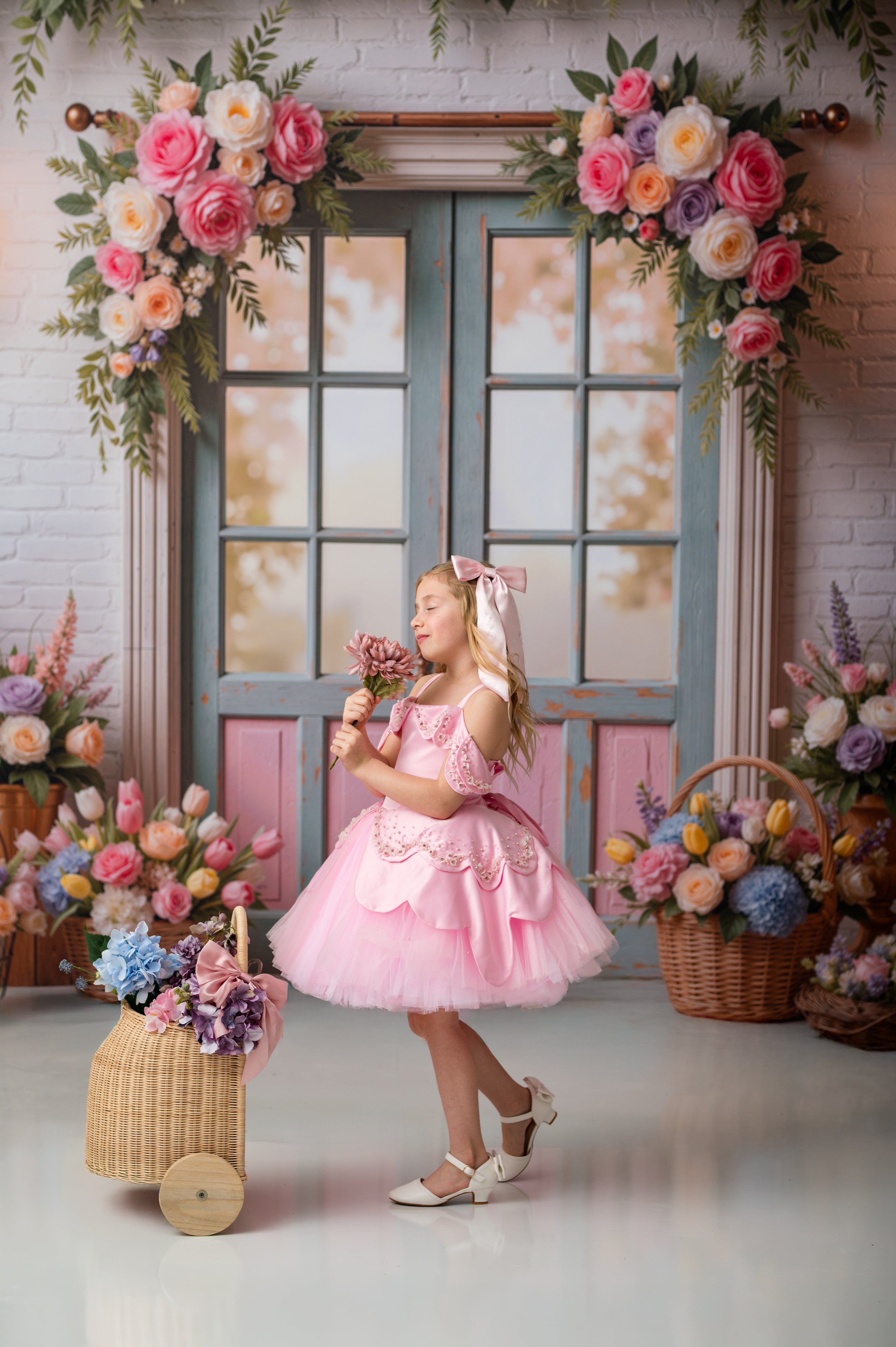 Young girl in a pink dress standing in front of a decorated door with floral arrangements.