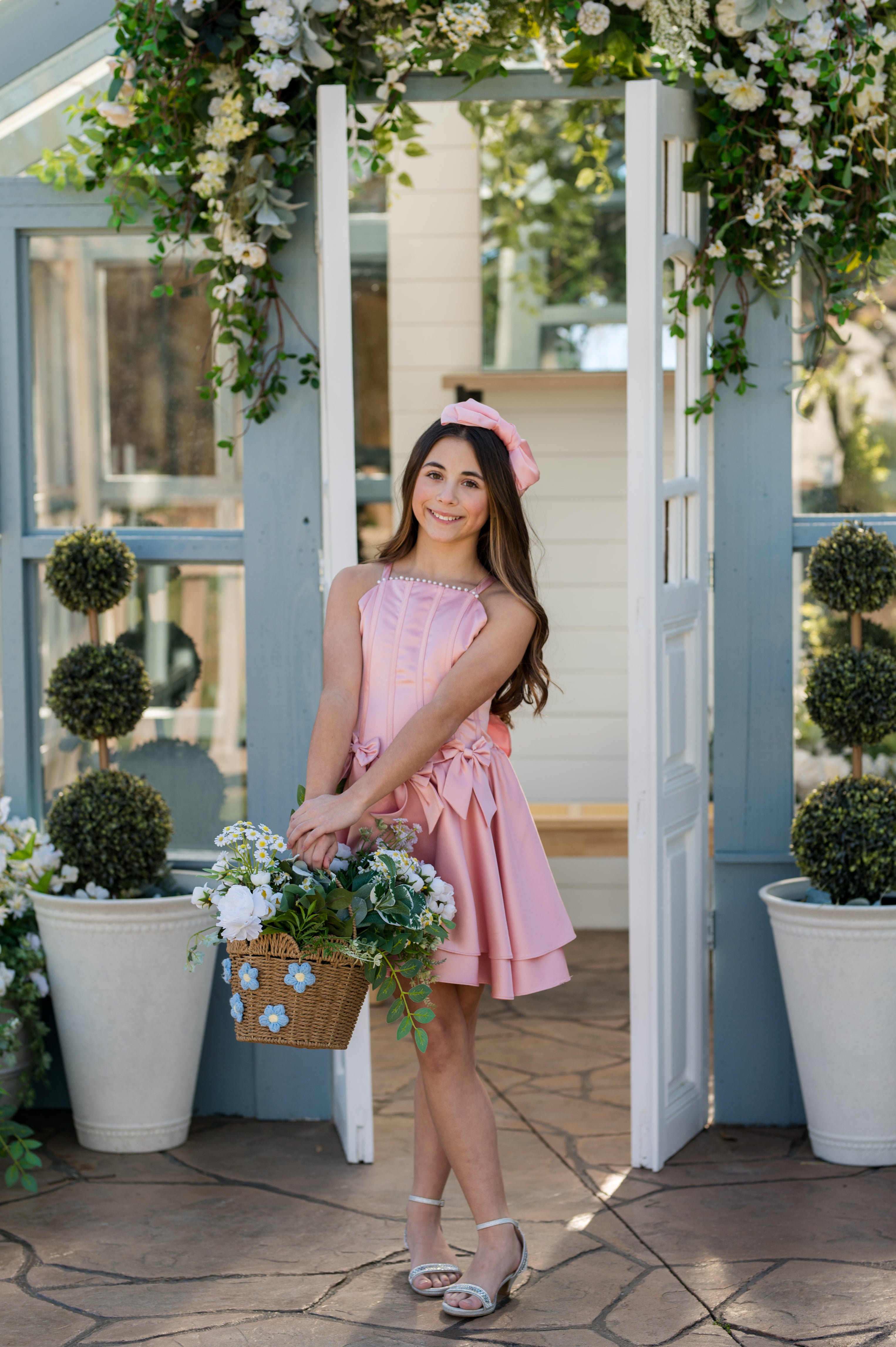 Young girl in a pink dress standing in front of a floral archway.