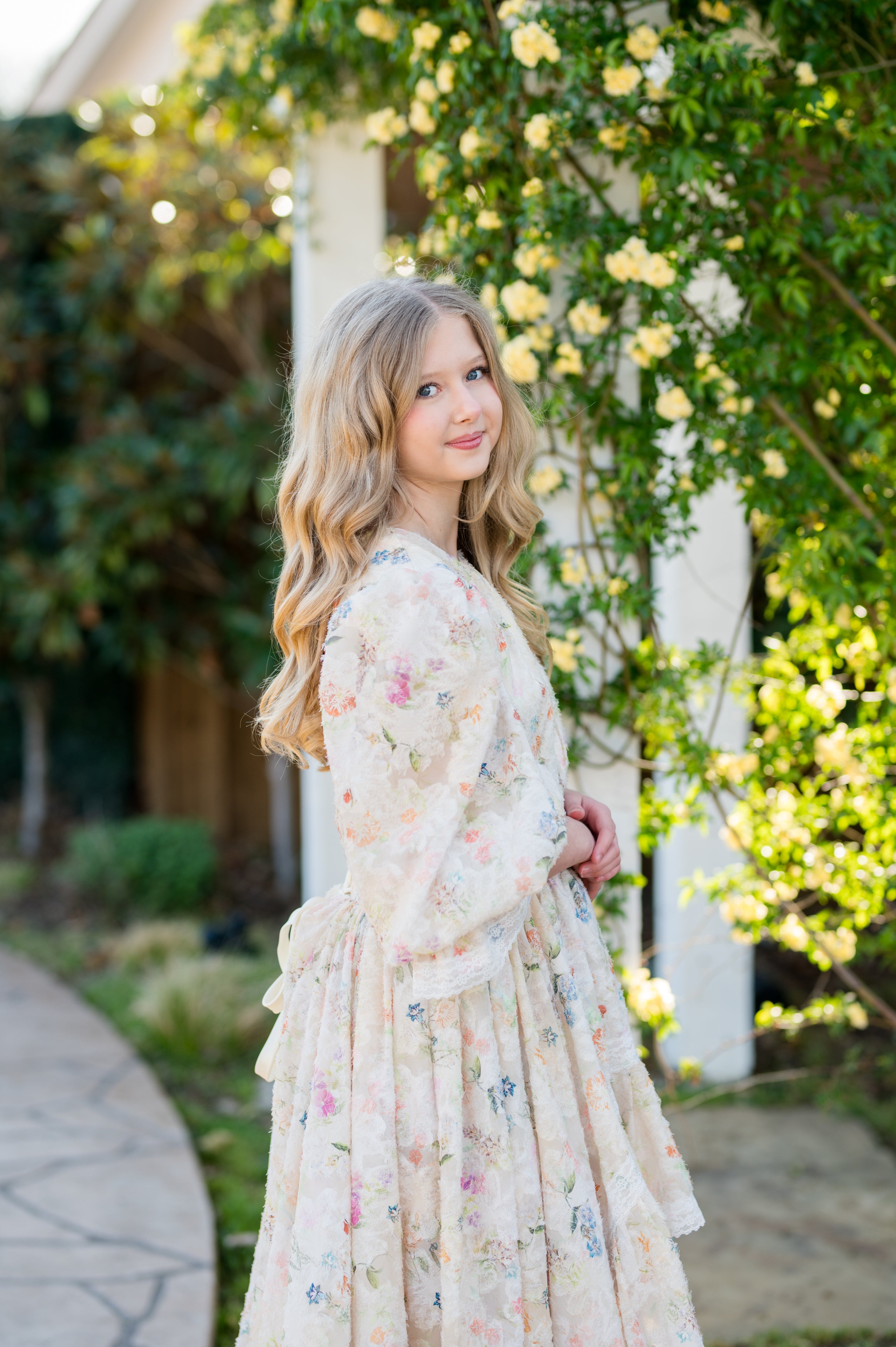 Woman in a floral dress standing in front of a white building with greenery
