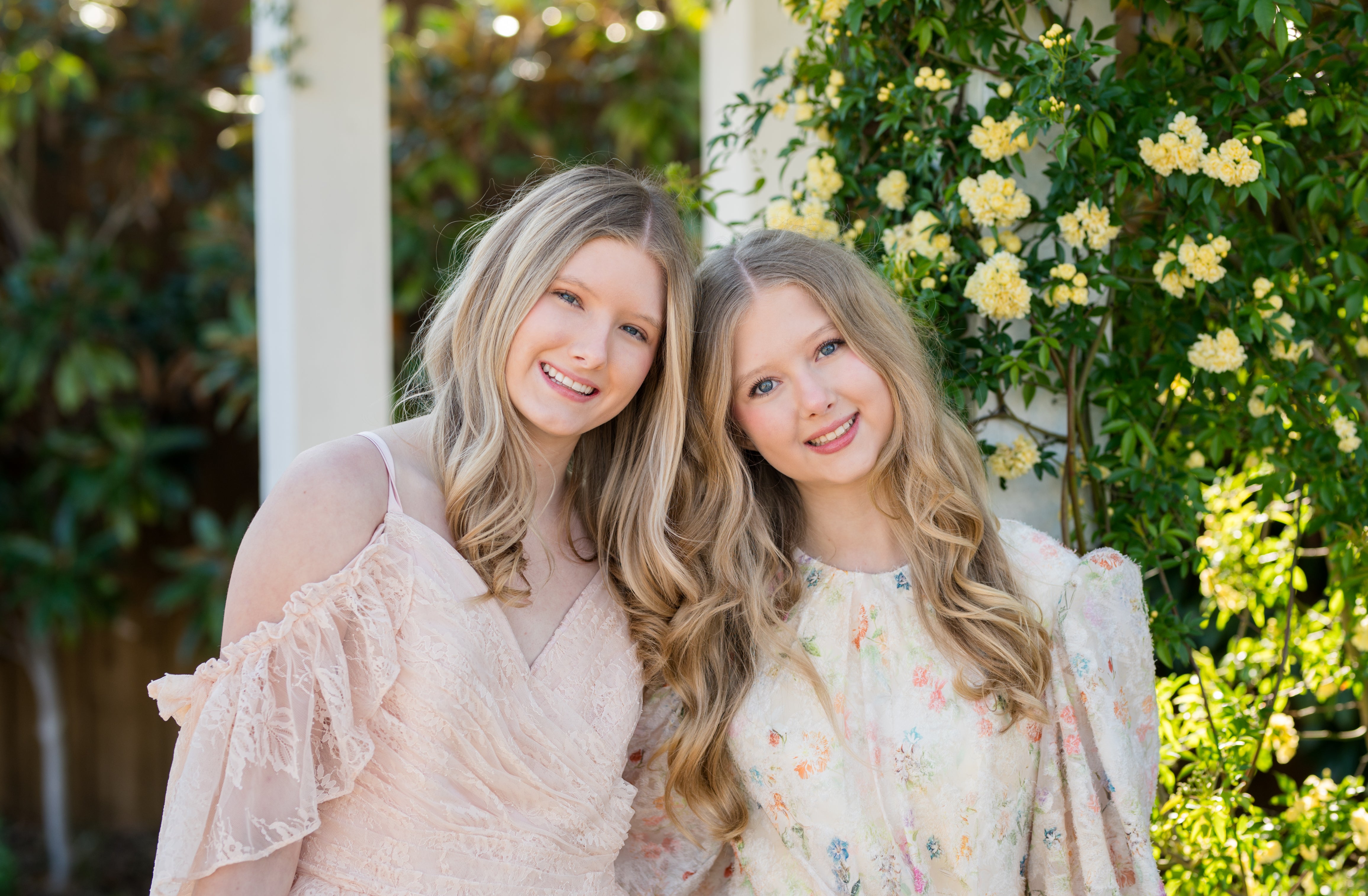 Two women standing together in a garden with greenery and flowers in the background