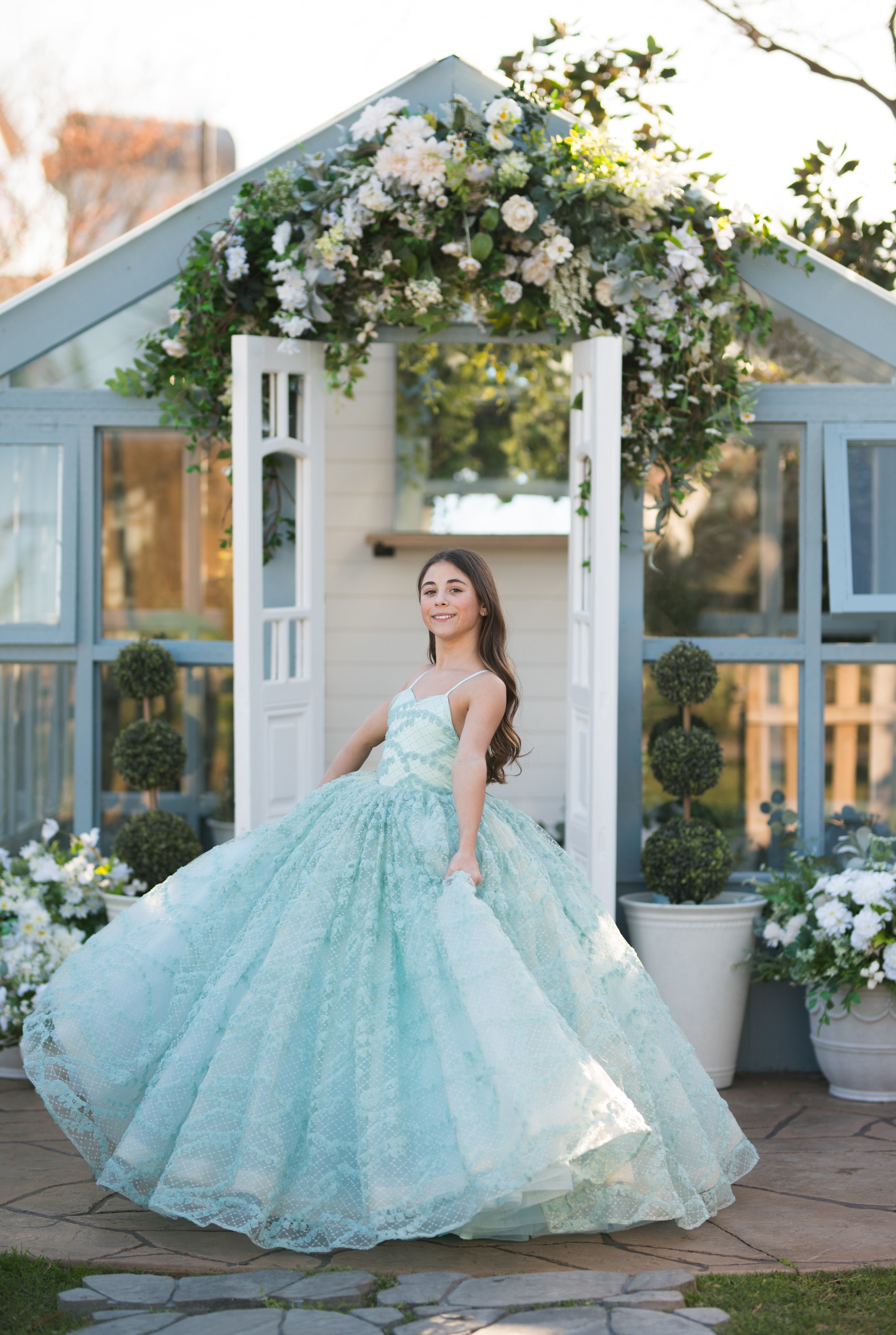 Woman in a light blue dress standing in front of a decorated archway with flowers.