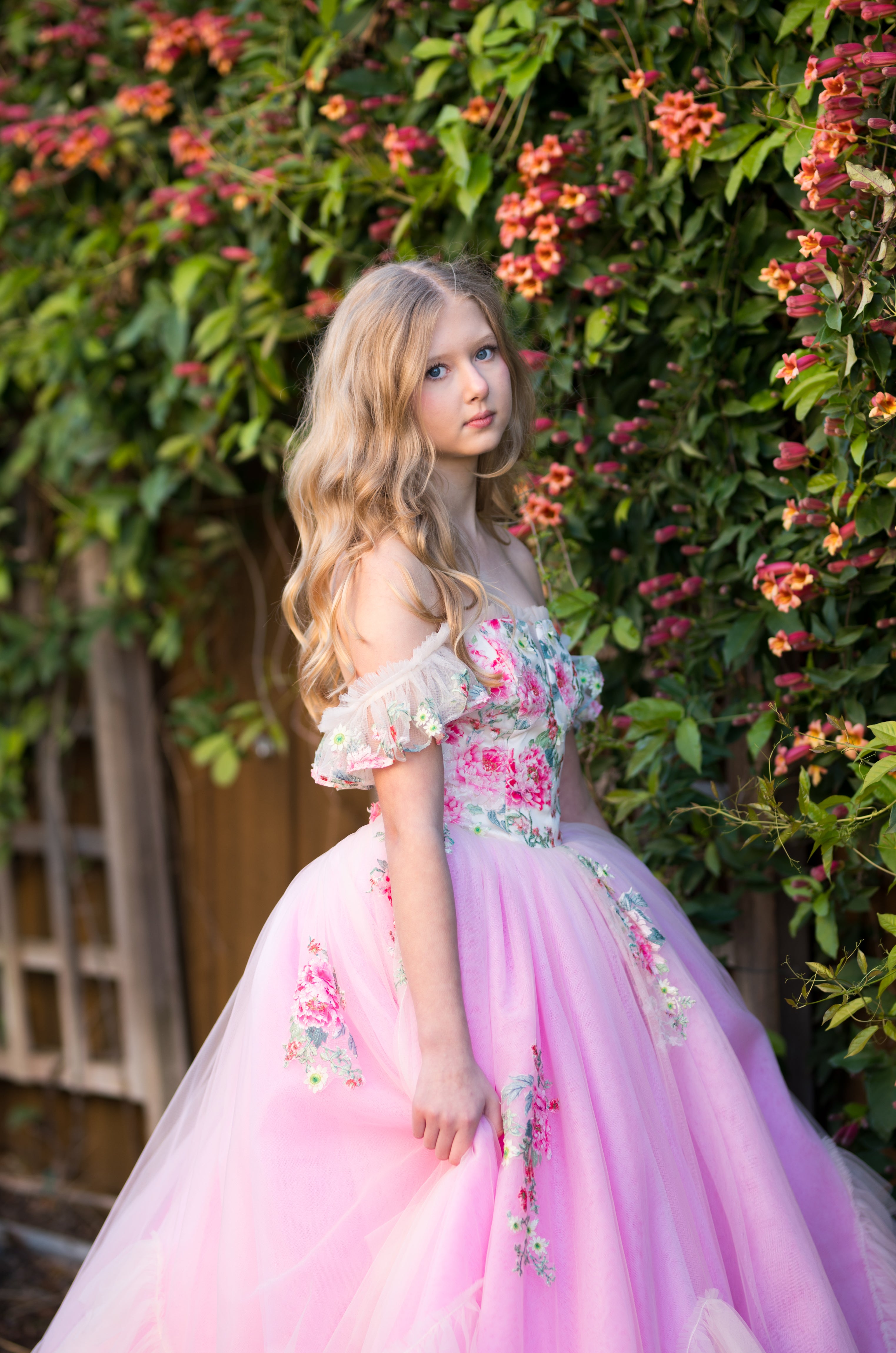 Young girl in a pink floral dress standing in front of a floral wall.
