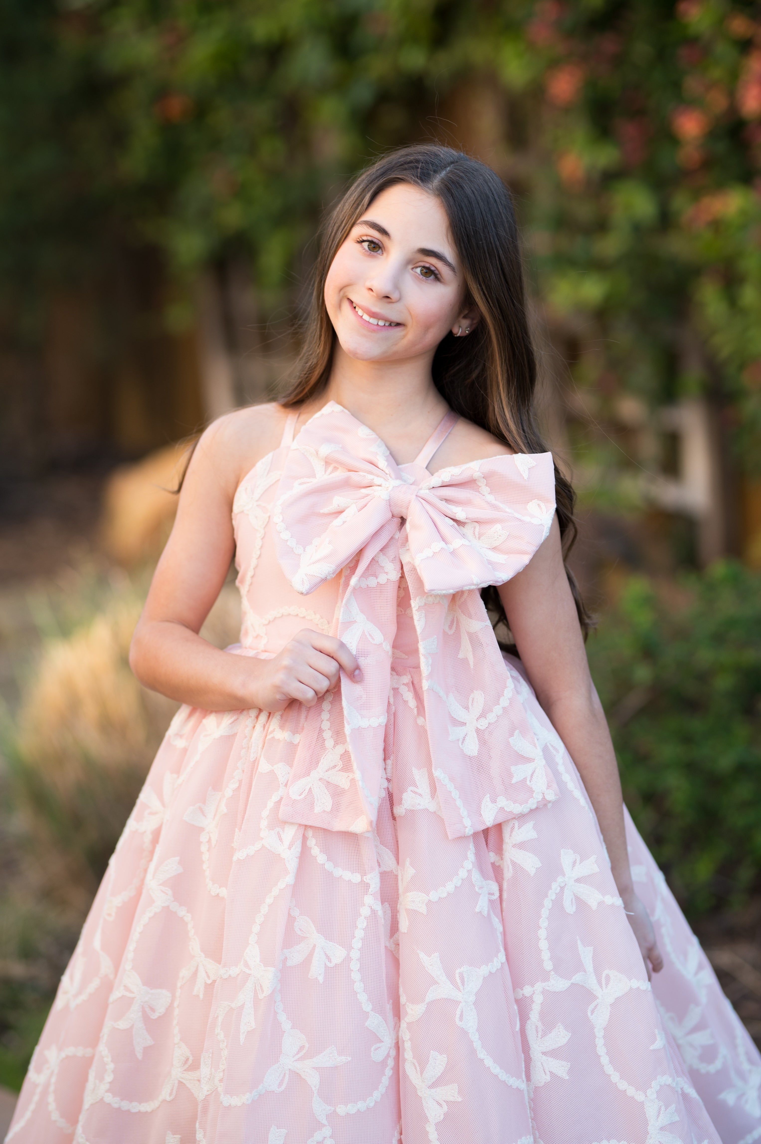 Young woman wearing a pink dress with a large bow in an outdoor setting