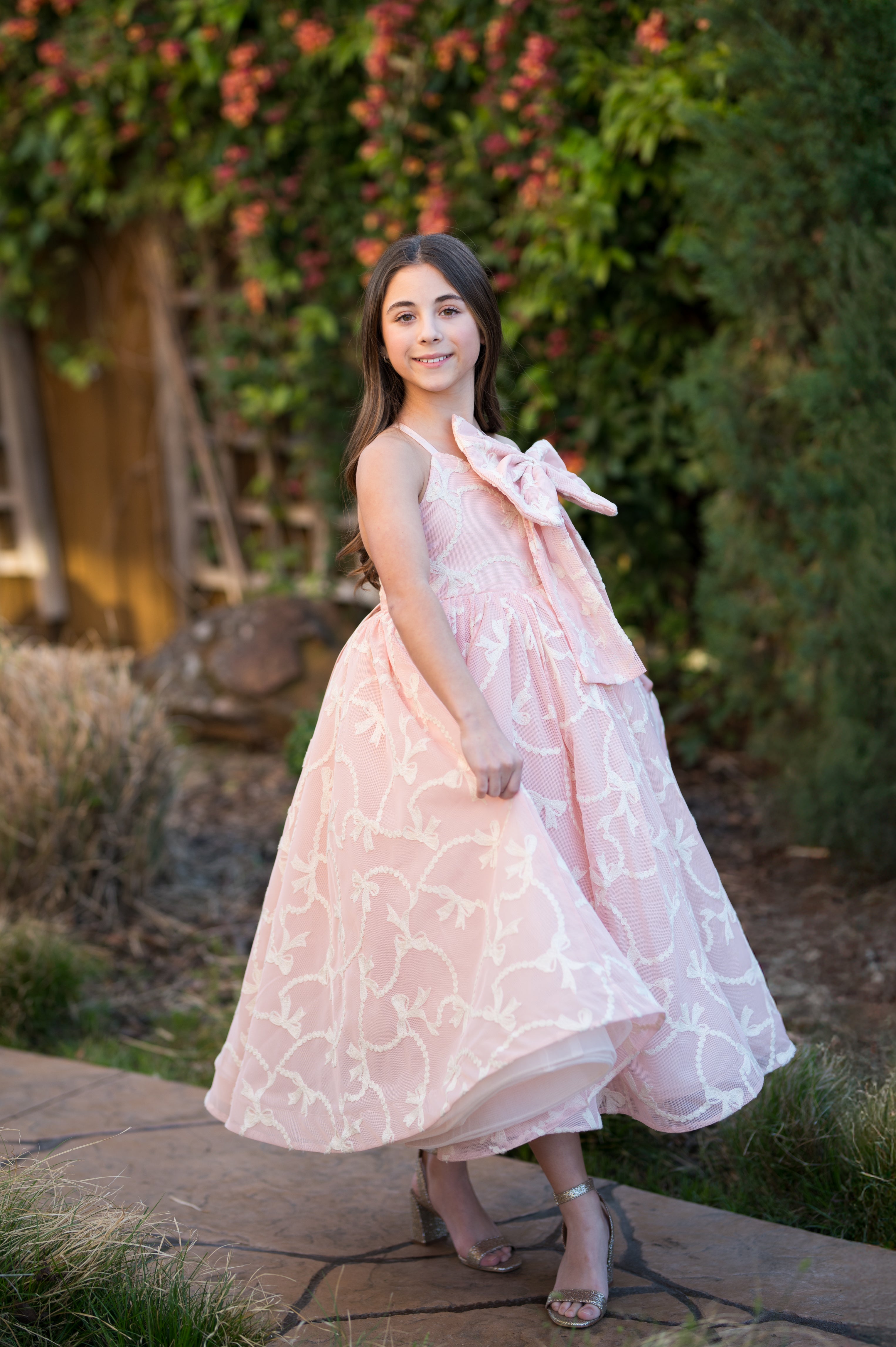 Woman in a pink floral dress standing outdoors with greenery in the background