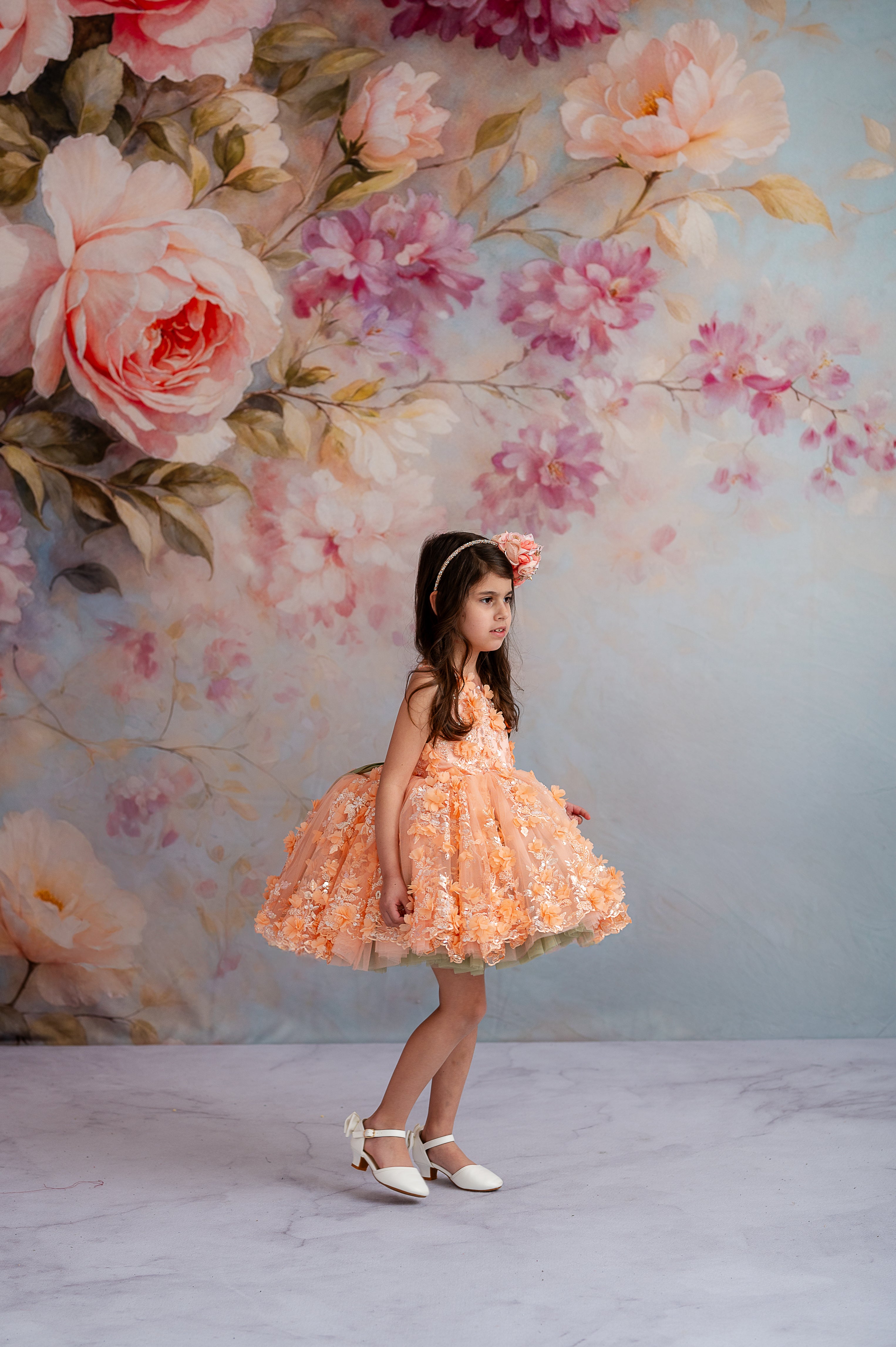 Girl wearing a vintage inspired dress with soft peach tones, floral embroidery, and petal-length skirt.