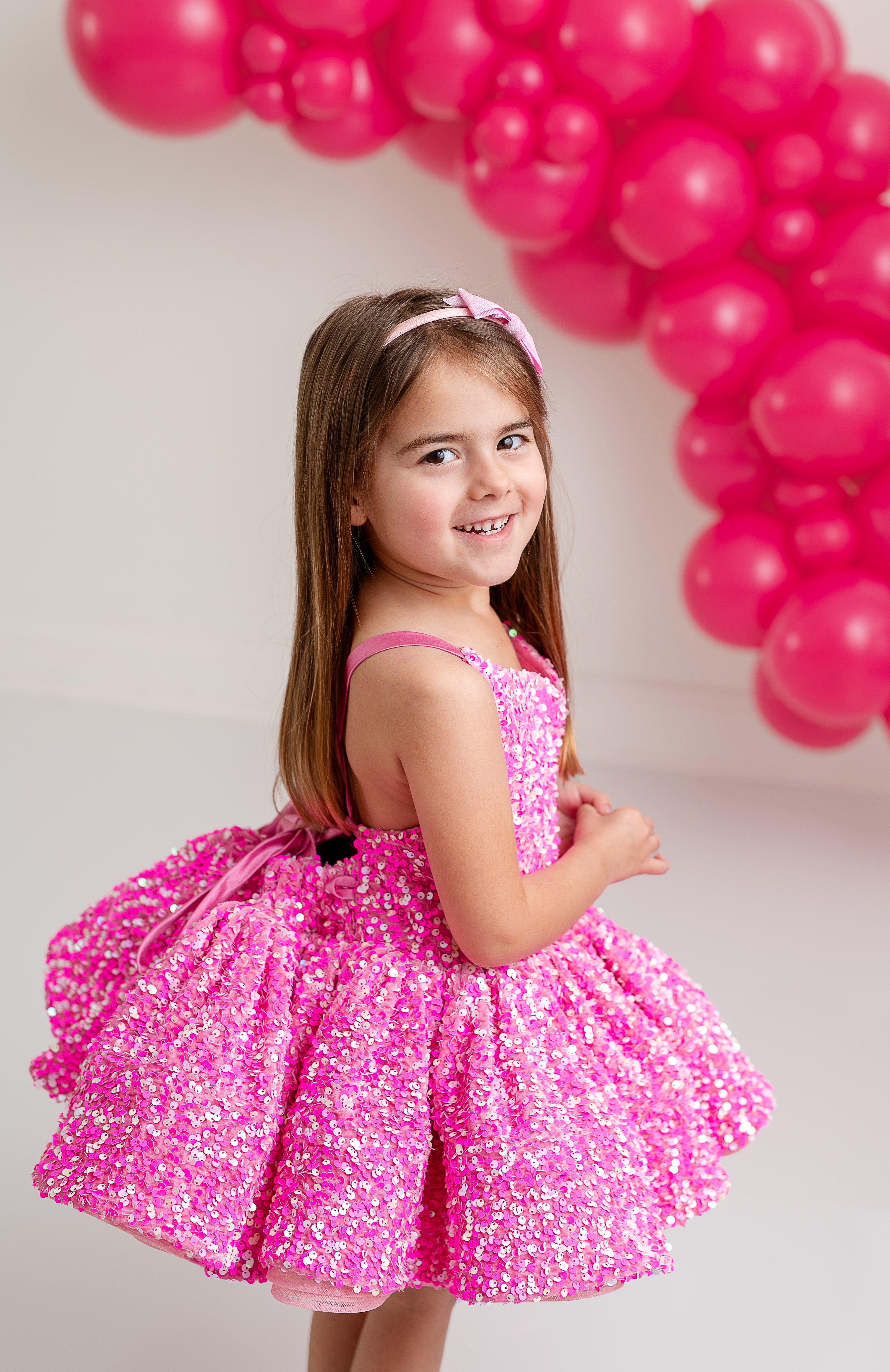 "Smiling girl in a sparkly pink dress with rainbow accents, dancing at a special event."