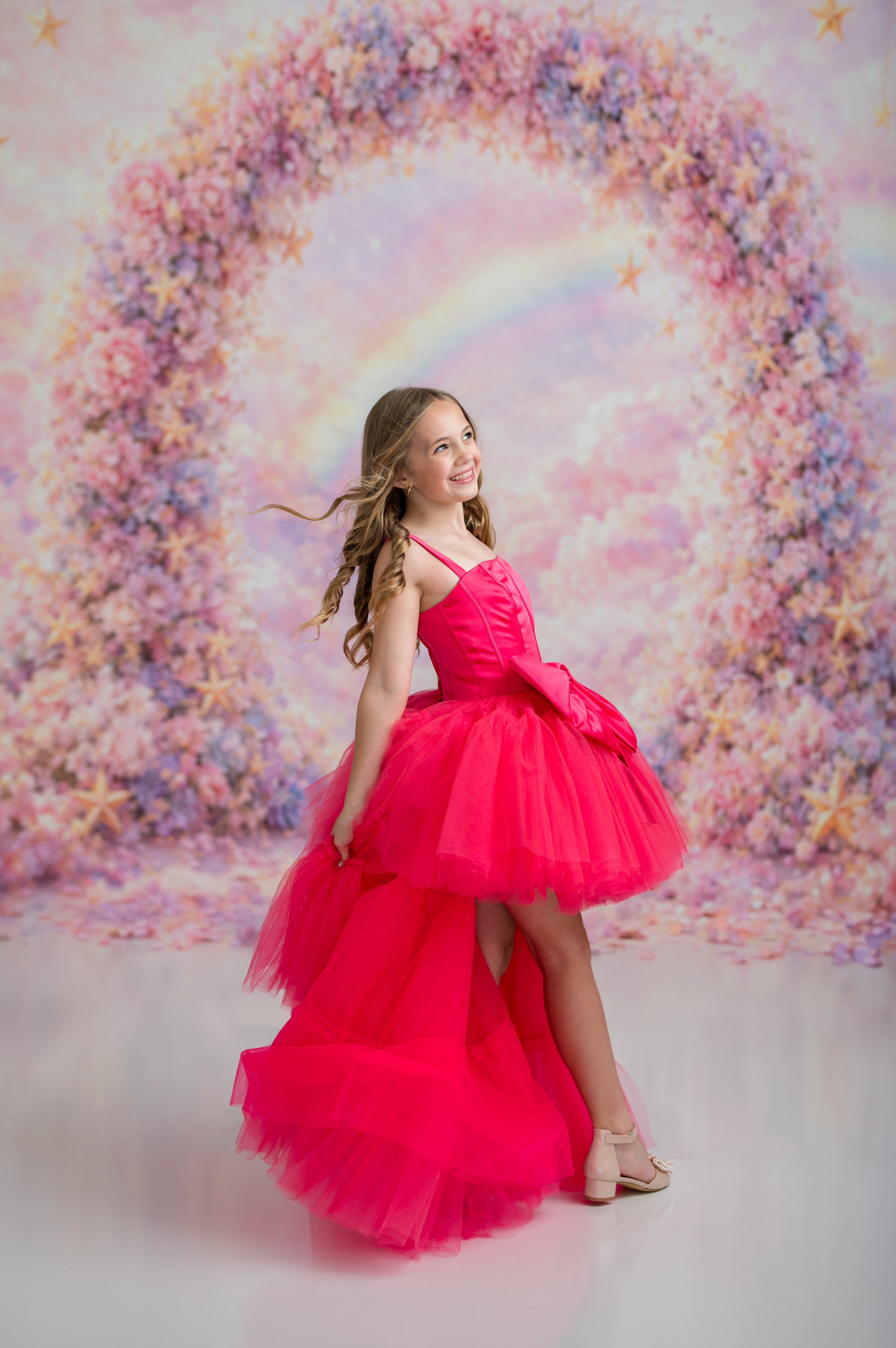 Young girl in a pink dress standing in front of a floral arch
