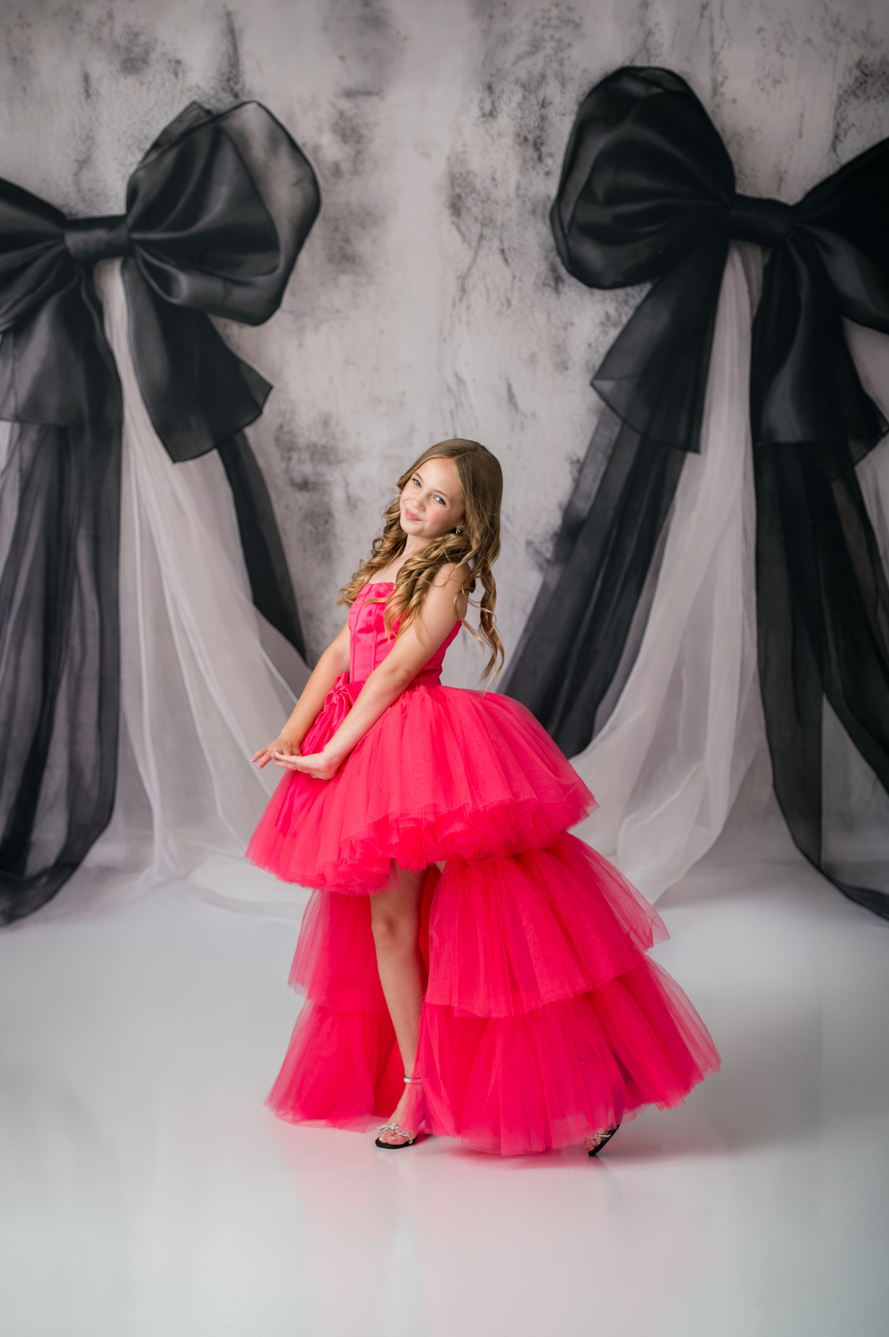 Young girl in a pink dress standing in front of large black bows on a gray background