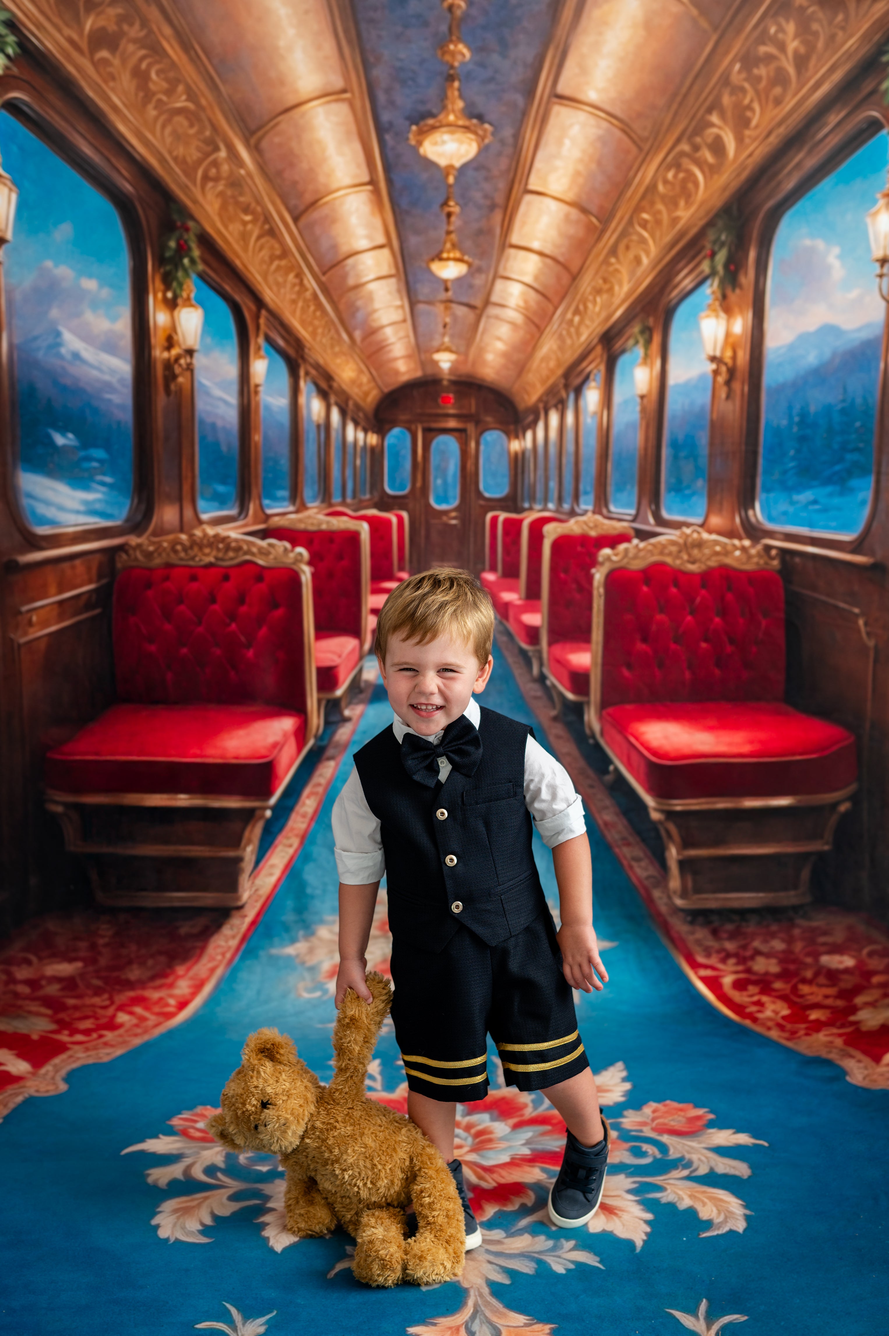 Young boy in a train car with red seats and ornate decor, holding a teddy bear.