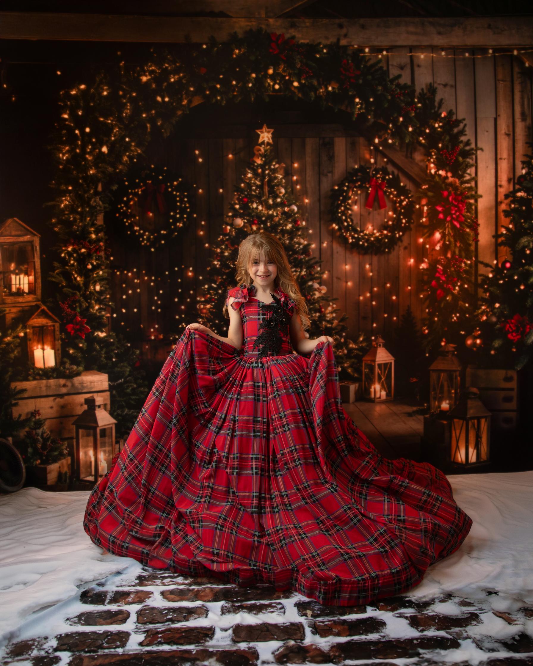 Little girl in a red plaid gown holding out the skirt, with twinkling lights and a Christmas tree in the background.