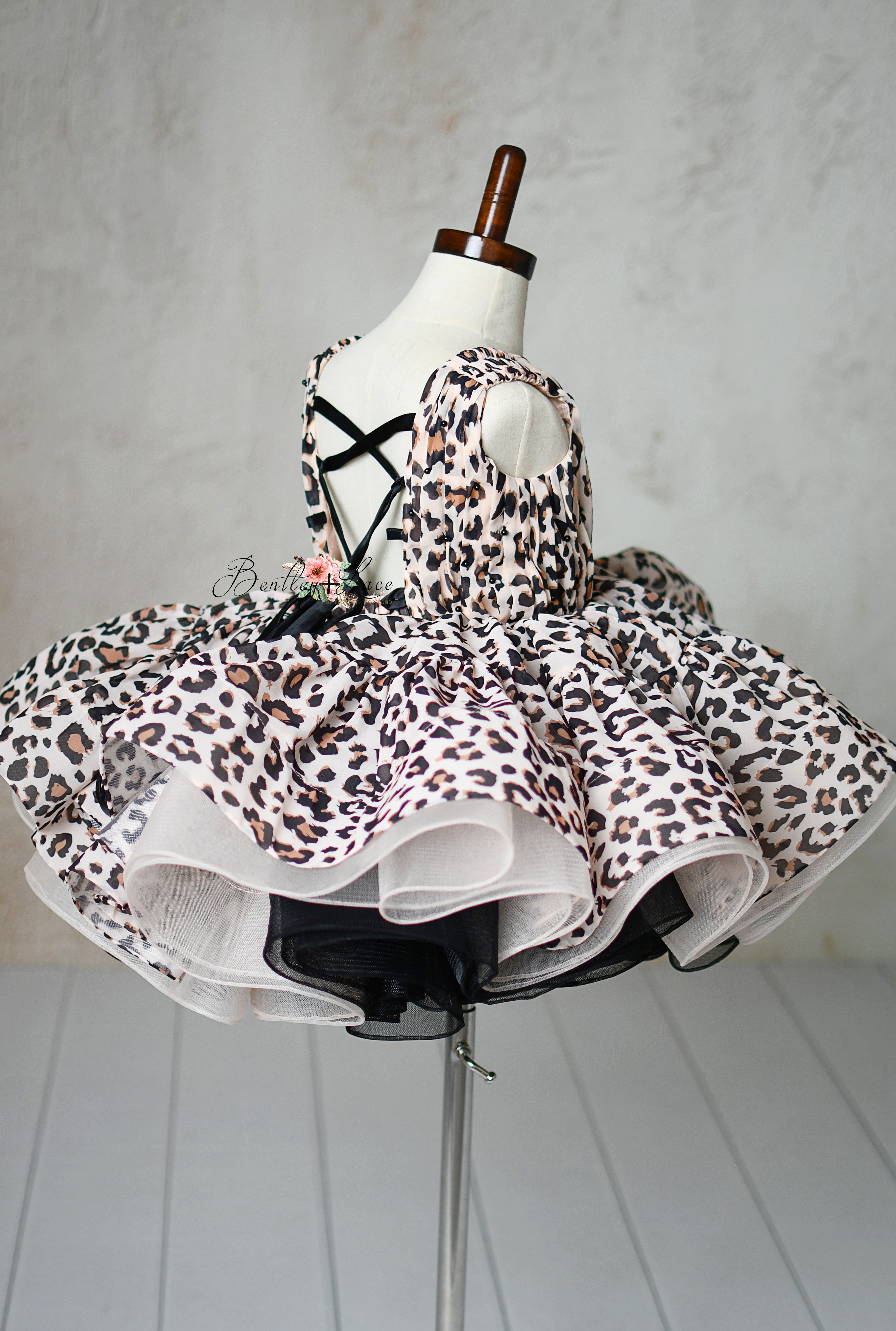 "Back view of a toddler-sized leopard print dress with adjustable shoulder ties and puff sleeves."
