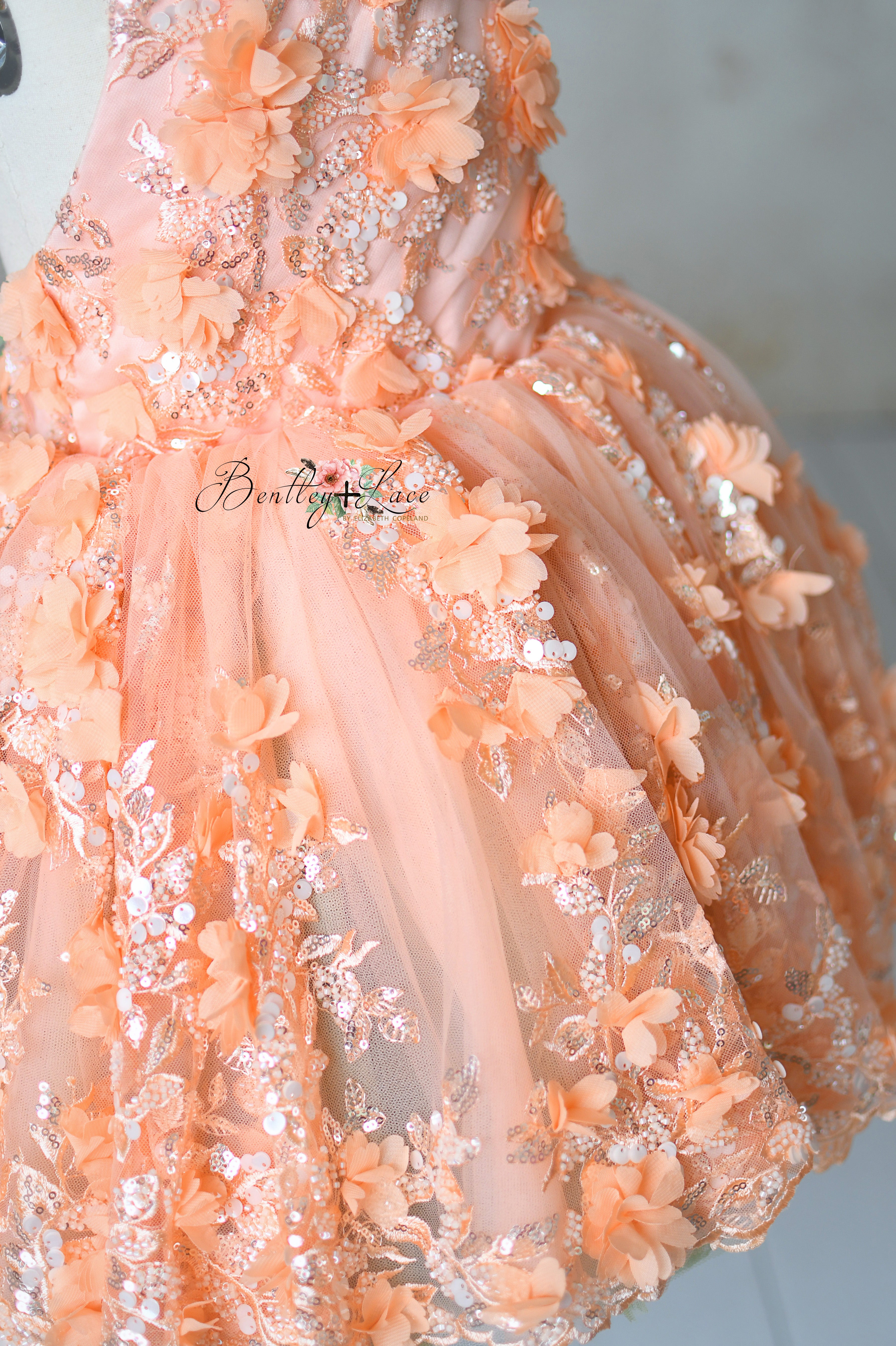 "Close-up of floral embroidery and soft peach fabric on the 'Peach Blossom' vintage petal-length dress for children."