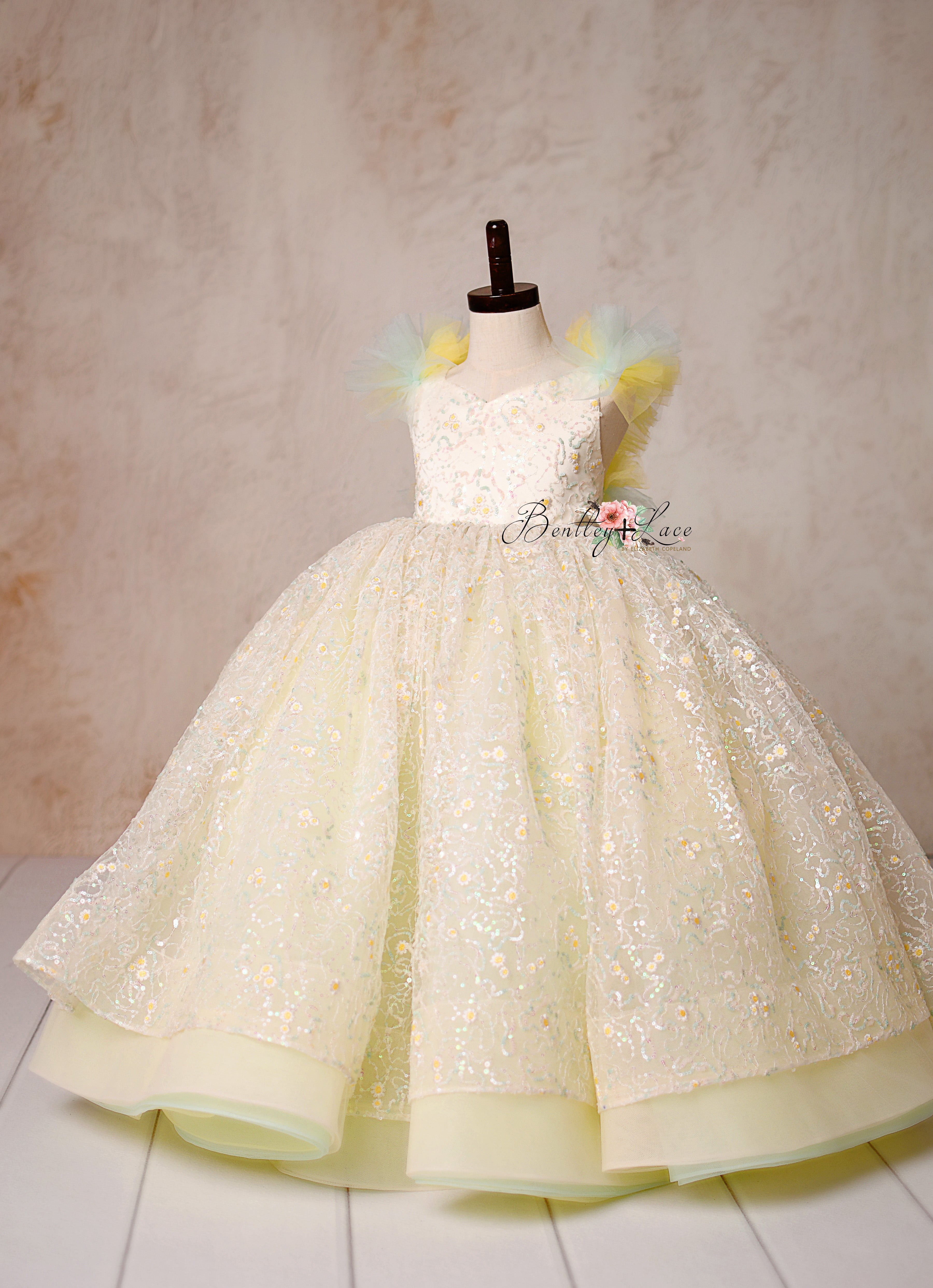 Capture timeless elegance with the Harmony Gown, featuring shimmering daisy lace, pastel hues, and a fairytale-inspired silhouette.
