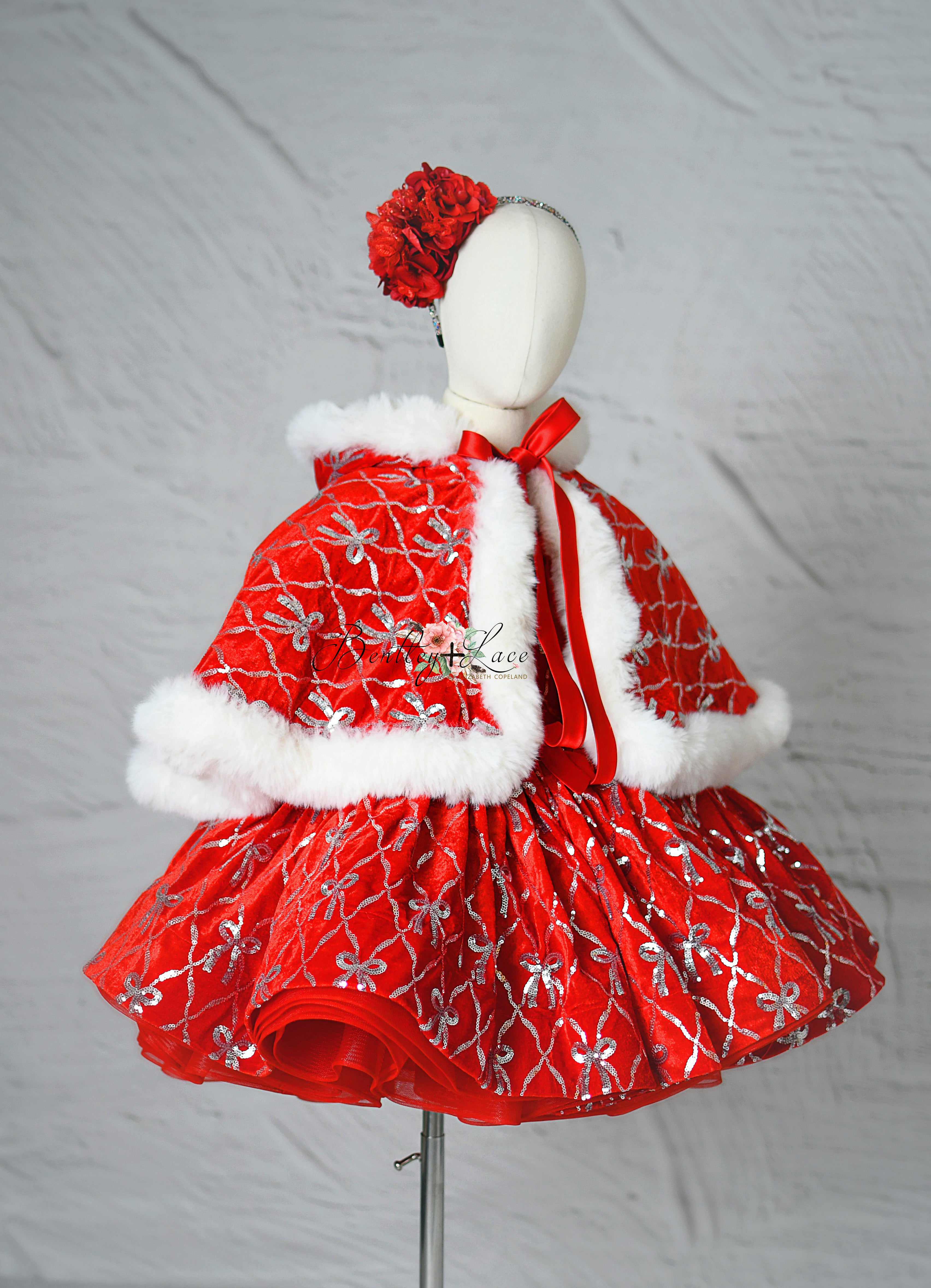 Red velvet holiday dress with silver embroidered bows and puff sleeves displayed on mannequin.