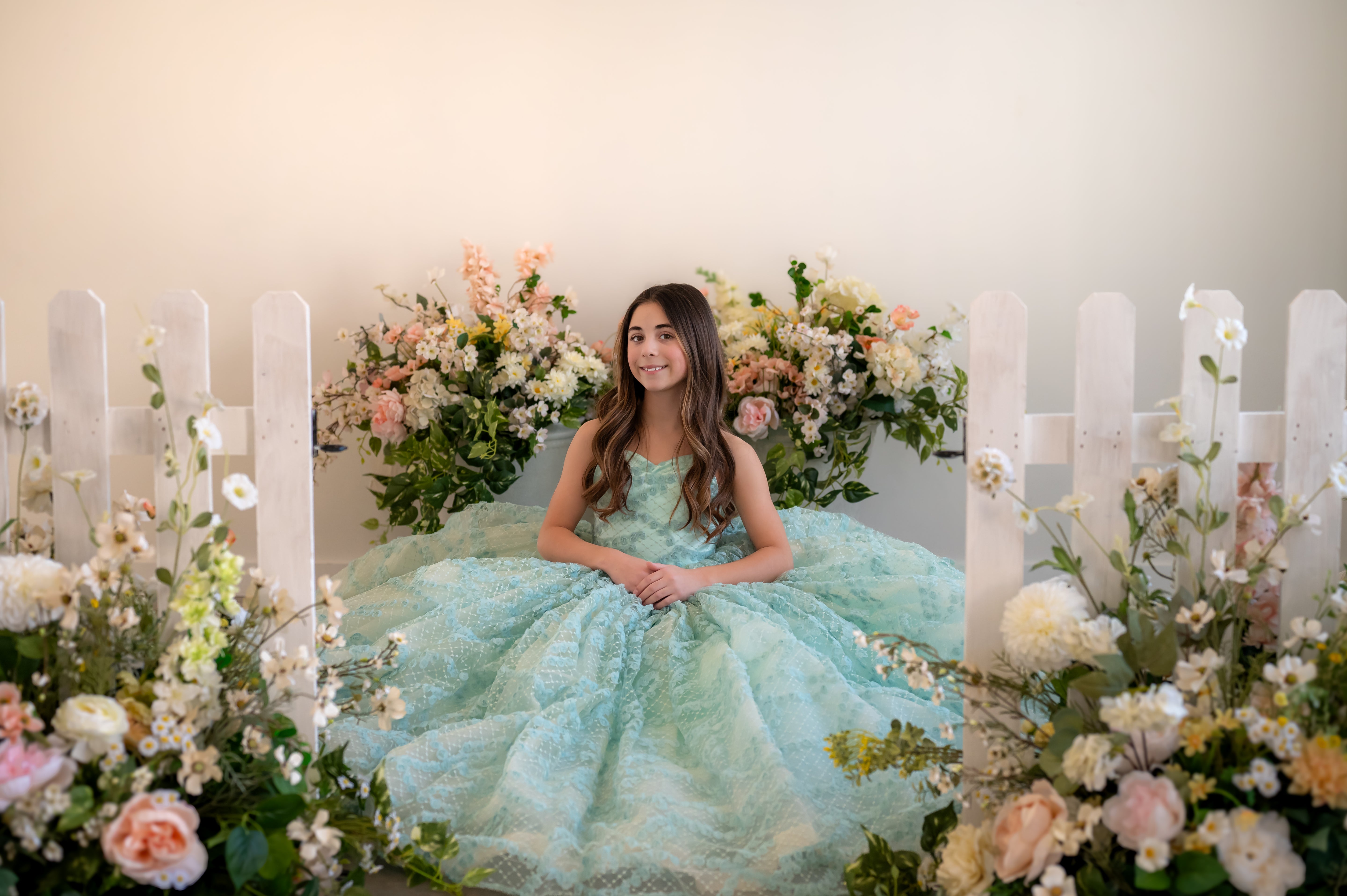 Woman in a light blue dress surrounded by flowers and candles in a decorated room.