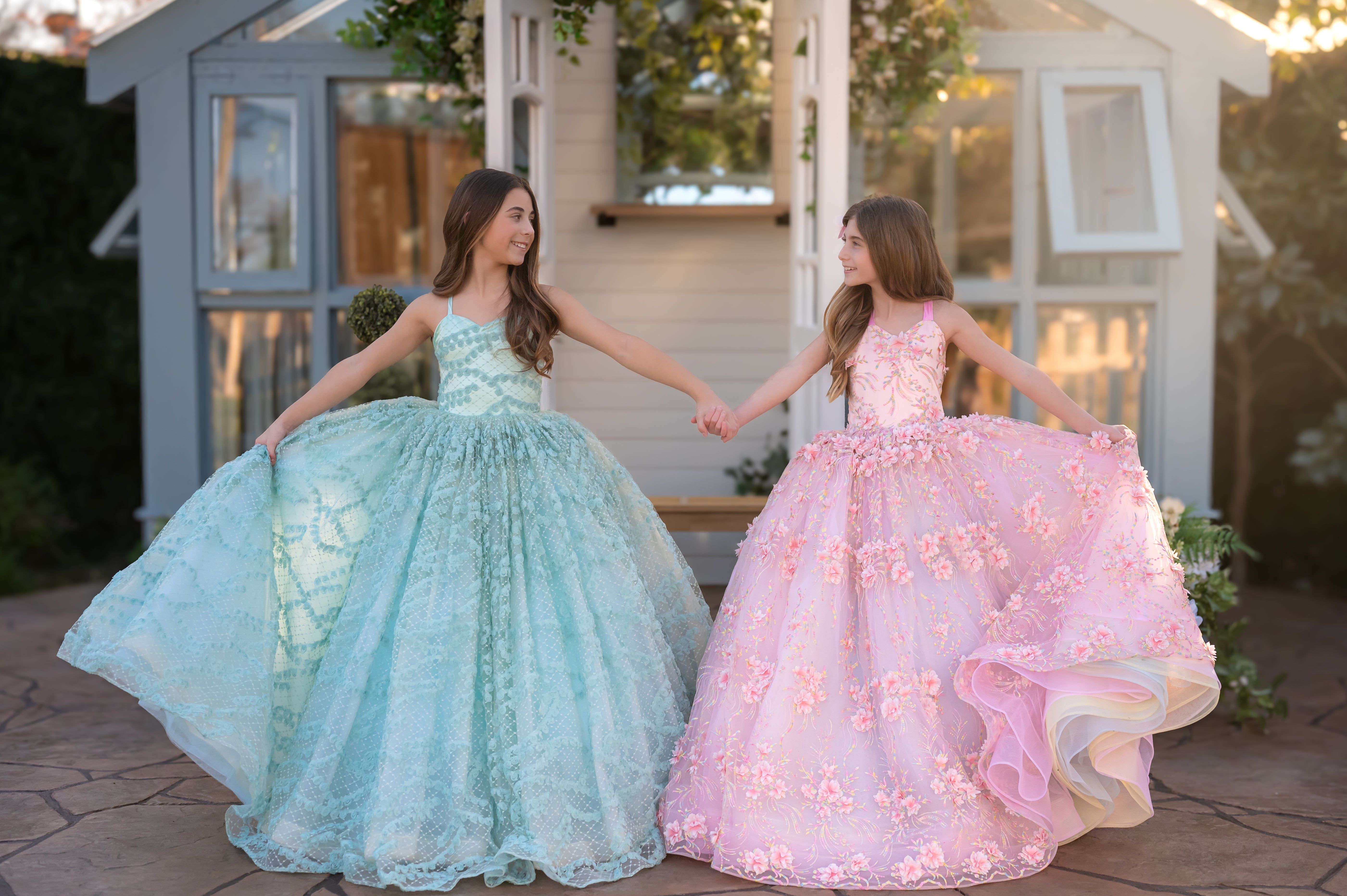 Two young girls in formal dresses holding hands outdoors.