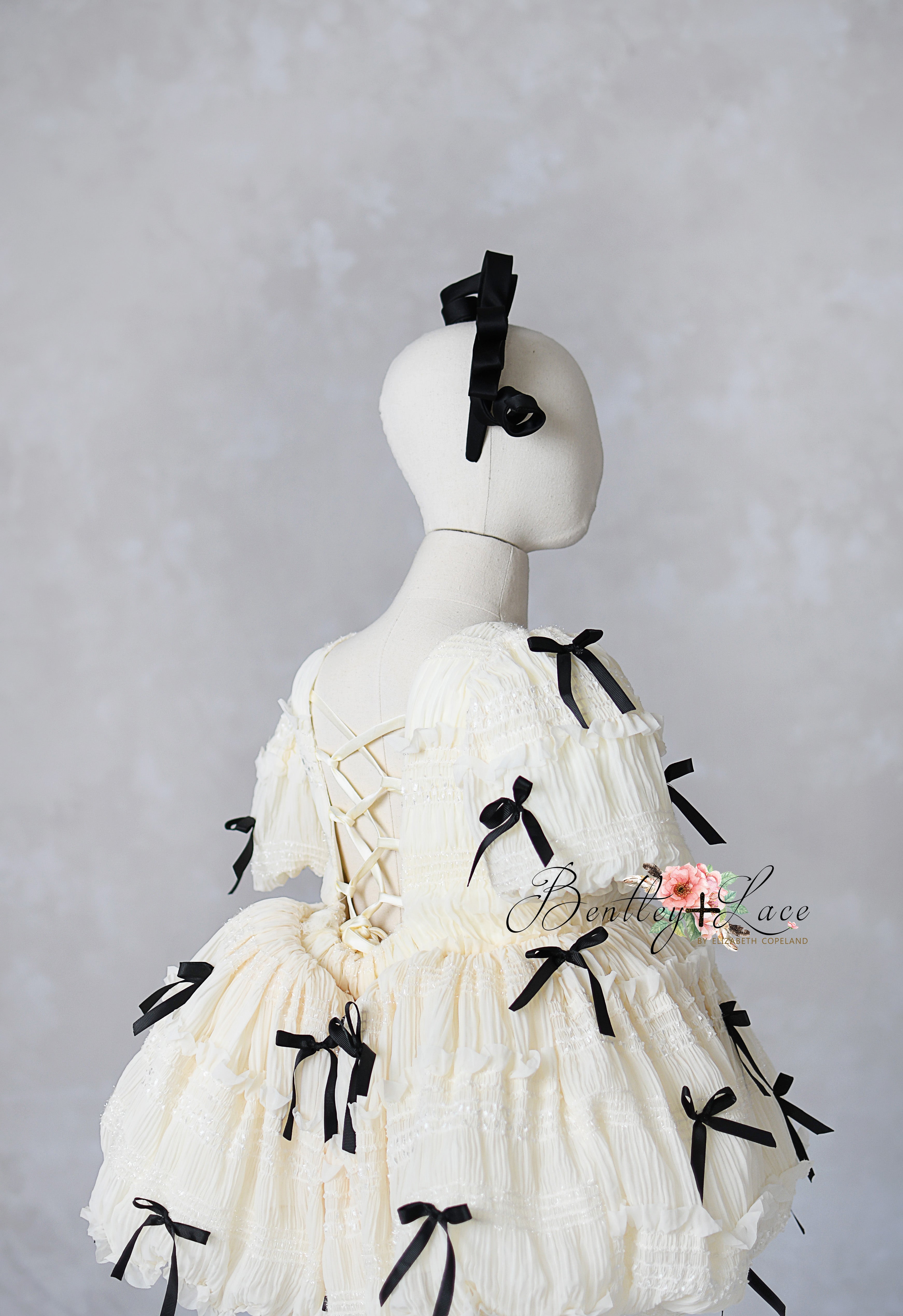 Luxury children's gown in cream with detachable sleeves and black ribbon accents, ideal for styled photo sessions.