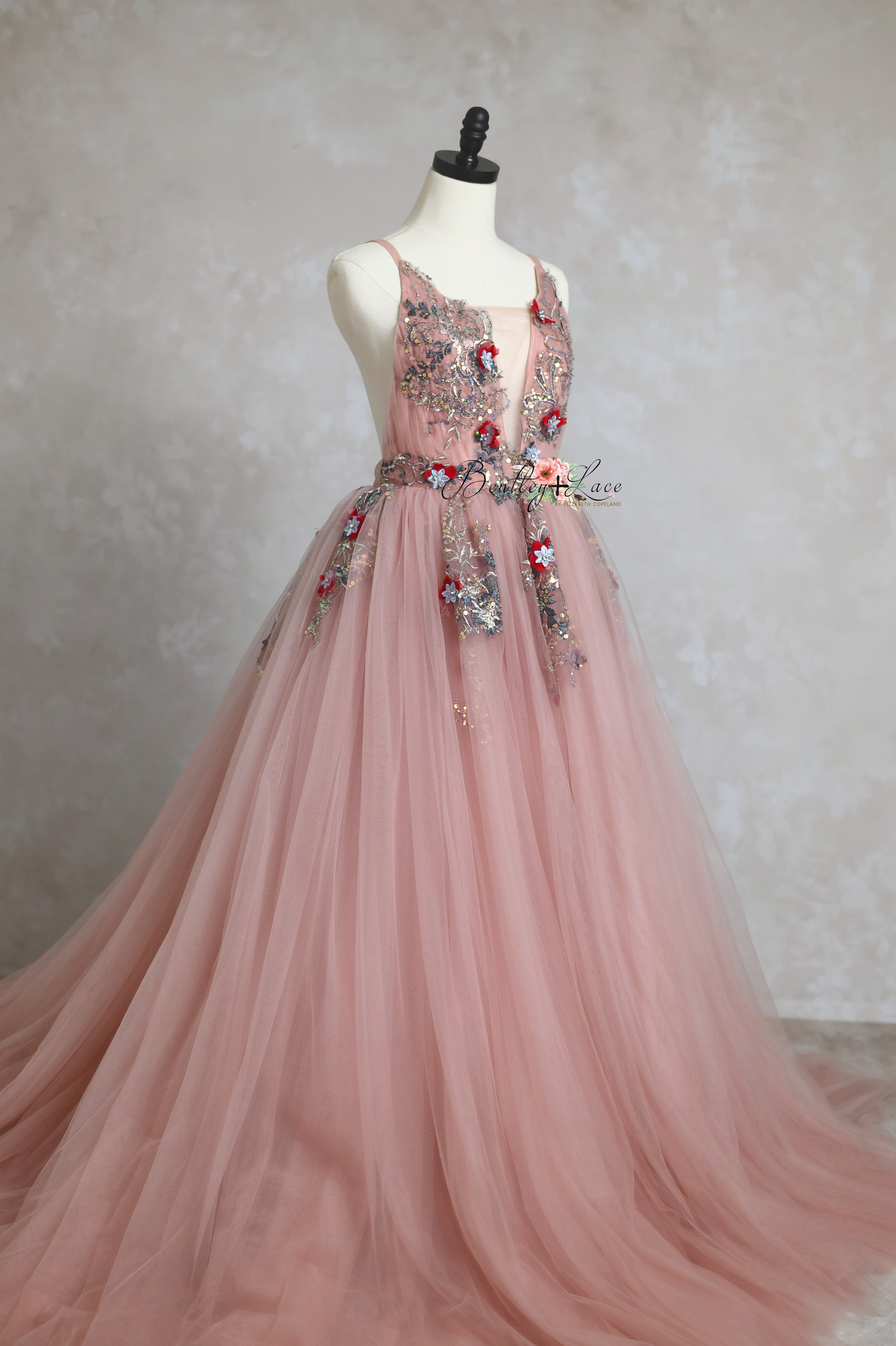 A bohemian-style Dillon gown in rose blush, featuring a deep V-cut bodice with floral appliques, a flexible back with shoulder ties, and a layered silk tulle skirt with an extended train